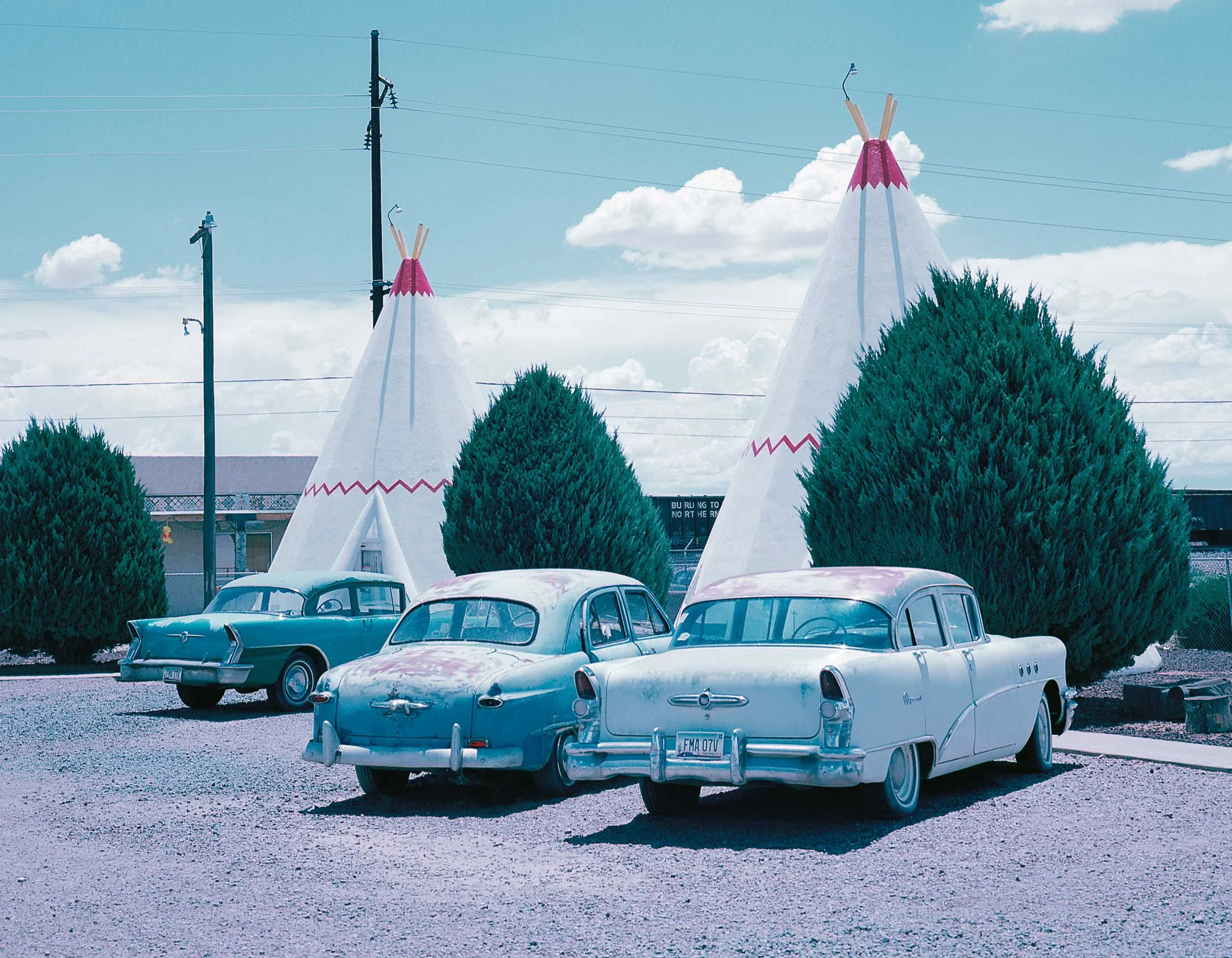 Three classic cars in front of teepees