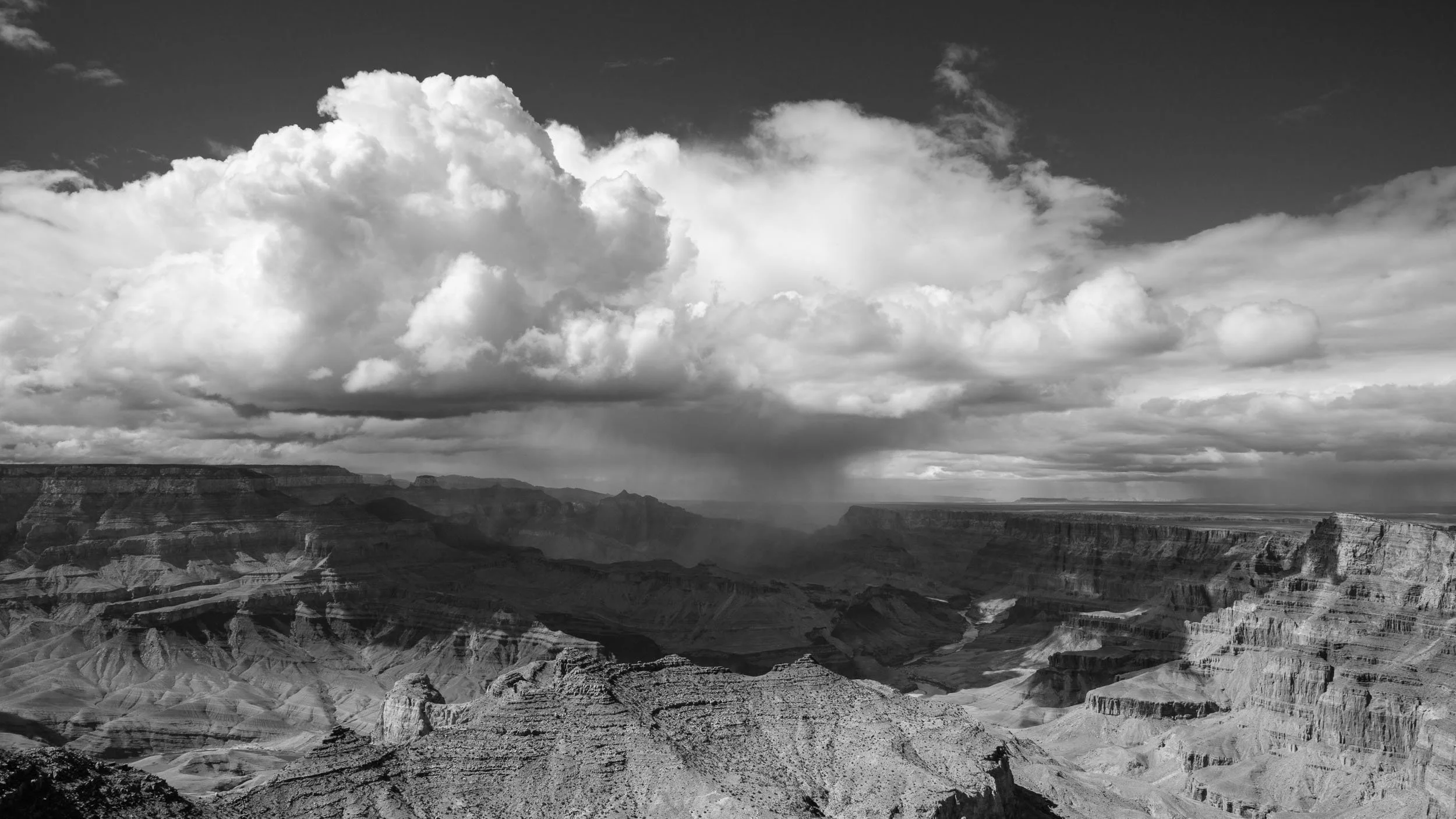 Black and white photograph of the Grand Canyon with dramatic clouds overhead.