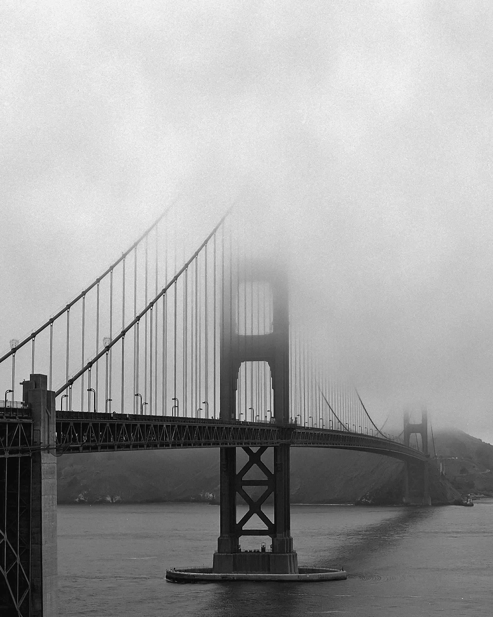 A black and white photo of the Golden Gate Bridge, with the bridge disappearing into fog clouds.