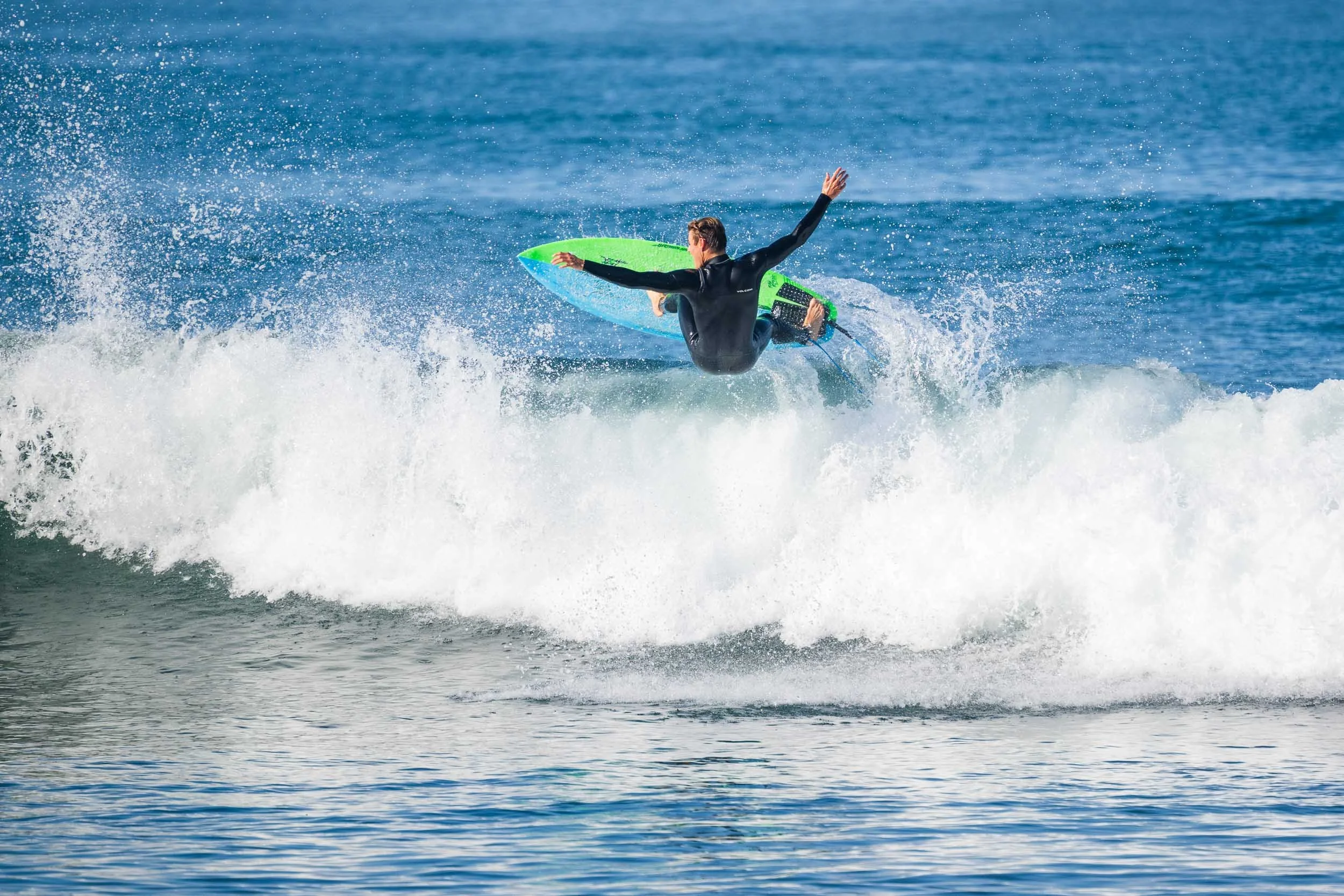 Person surfing on a bright green and blue surfboard riding a wave in the ocean.