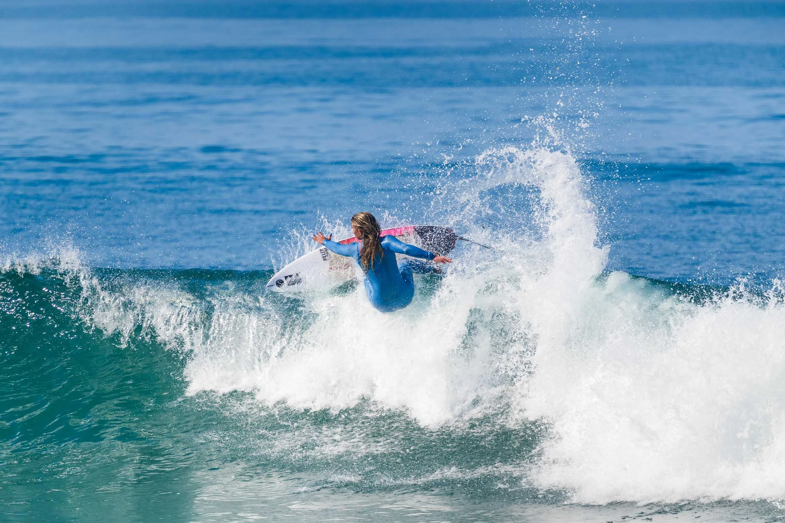 A young girl wearing a blue wetsuit surfing on a paddleboard in the ocean, surrounded by waves and splashes of water.