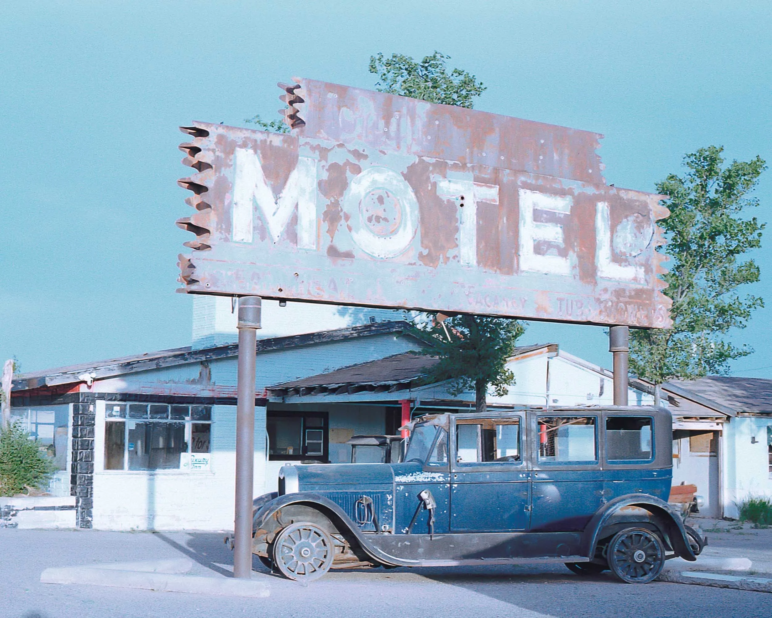 An old, rusty sign. A vintage vehicle is parked in front of the sign.