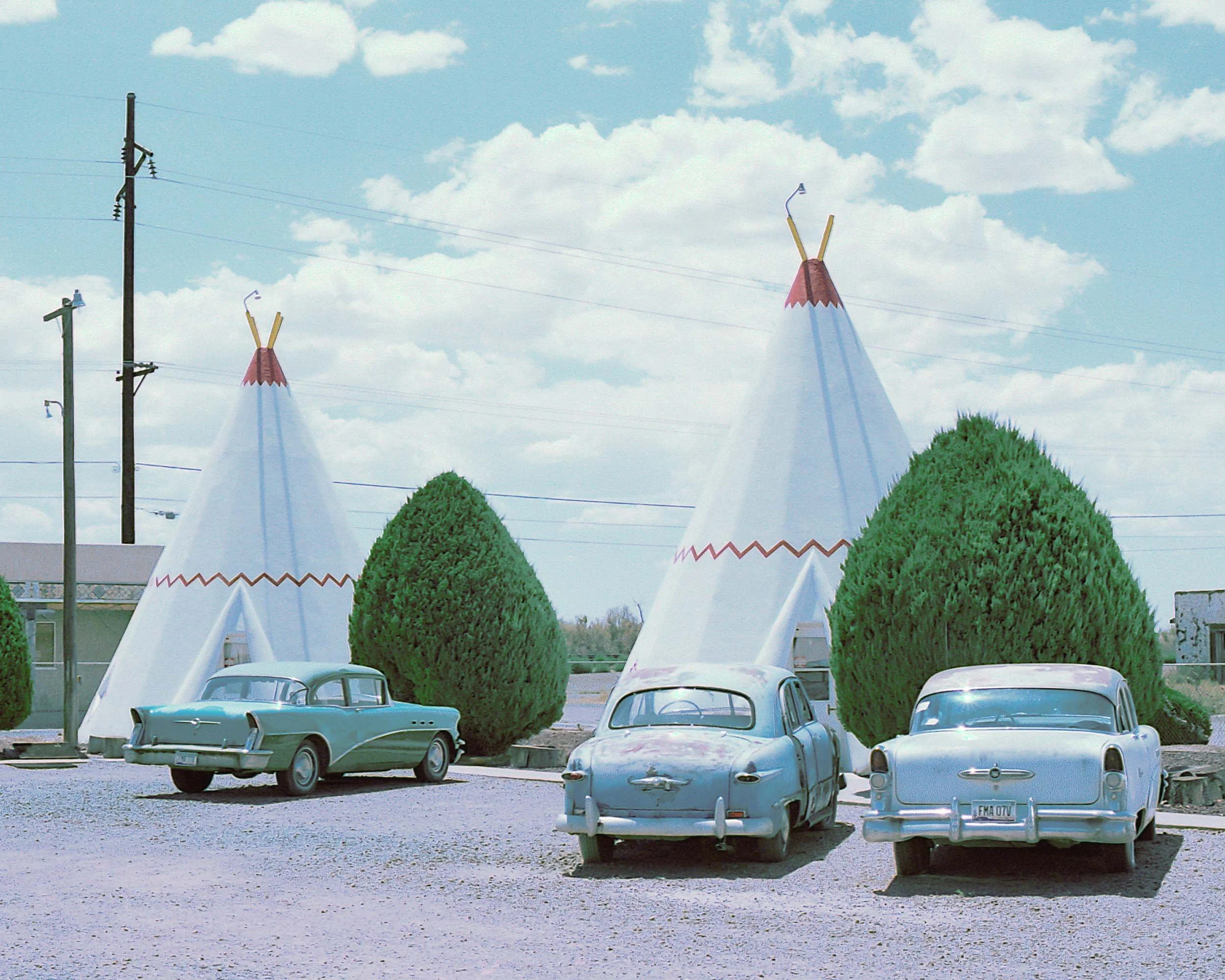 Vintage cars parked in front of a building with large white teepee-shaped structures 