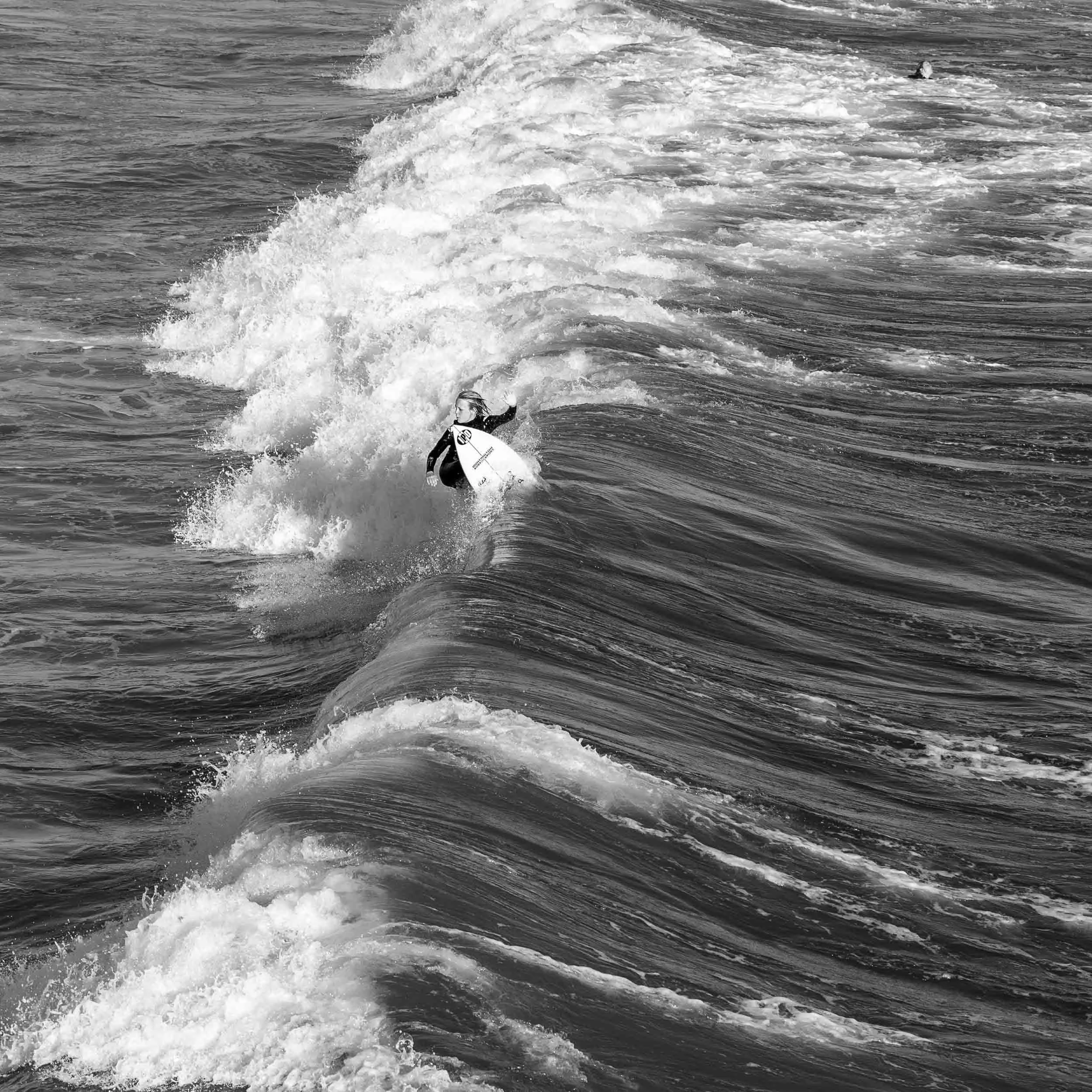 A person surfing on a surfboard on the ocean waves in black and white.