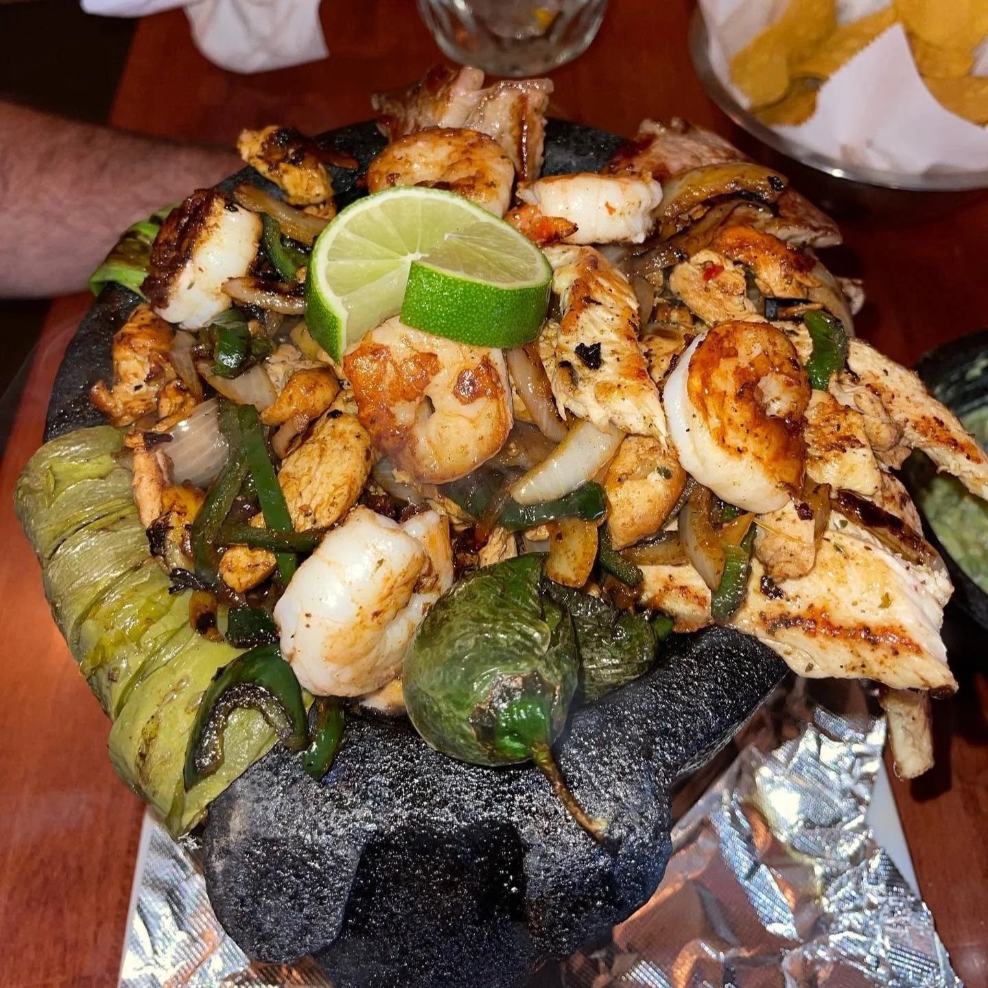 Grilled seafood platter topped with lime on a charred asphalt stone in a restaurant setting.