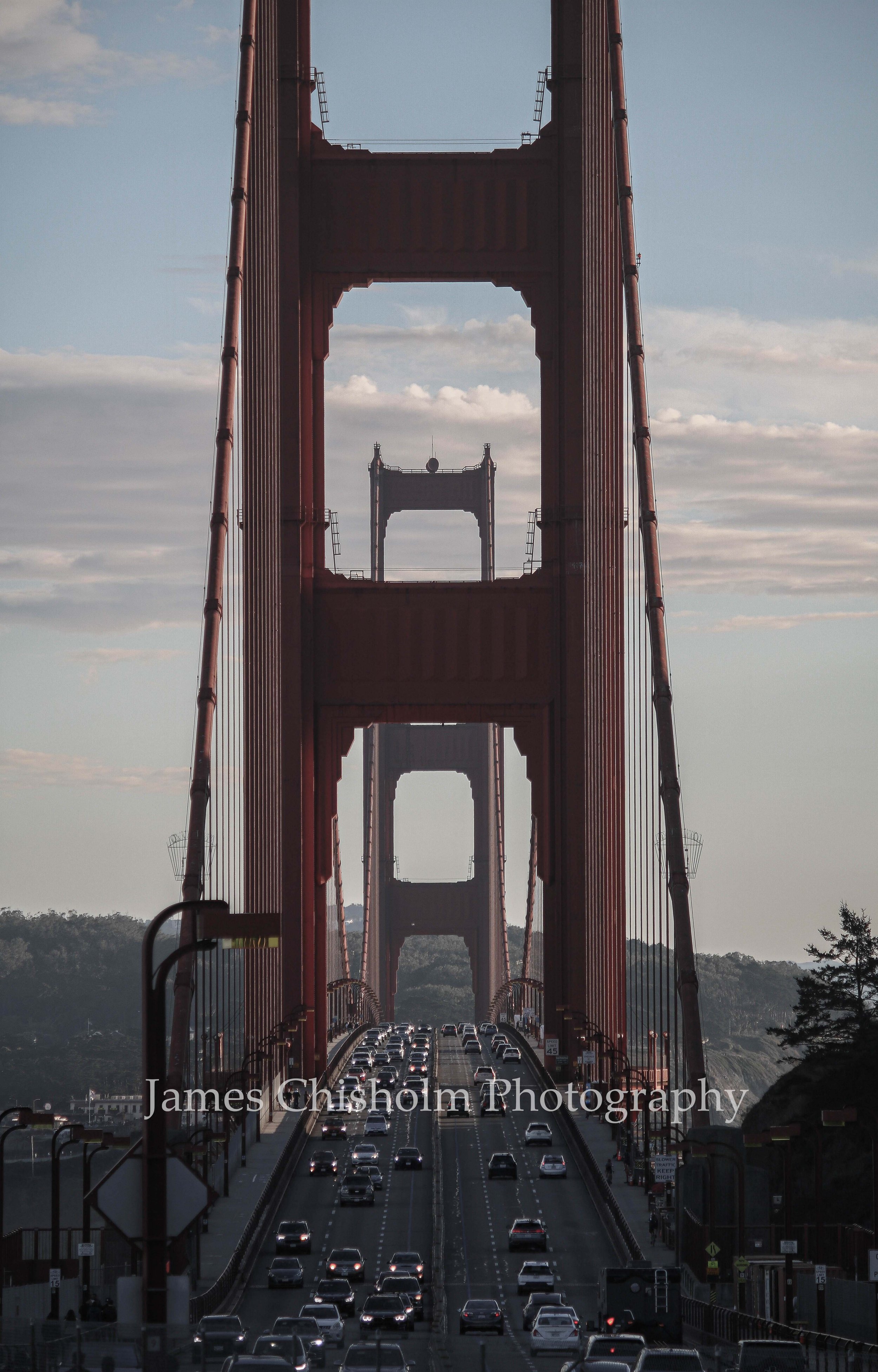View of the Golden Gate Bridge with cars driving on the road beneath it, and the sky filled with clouds.