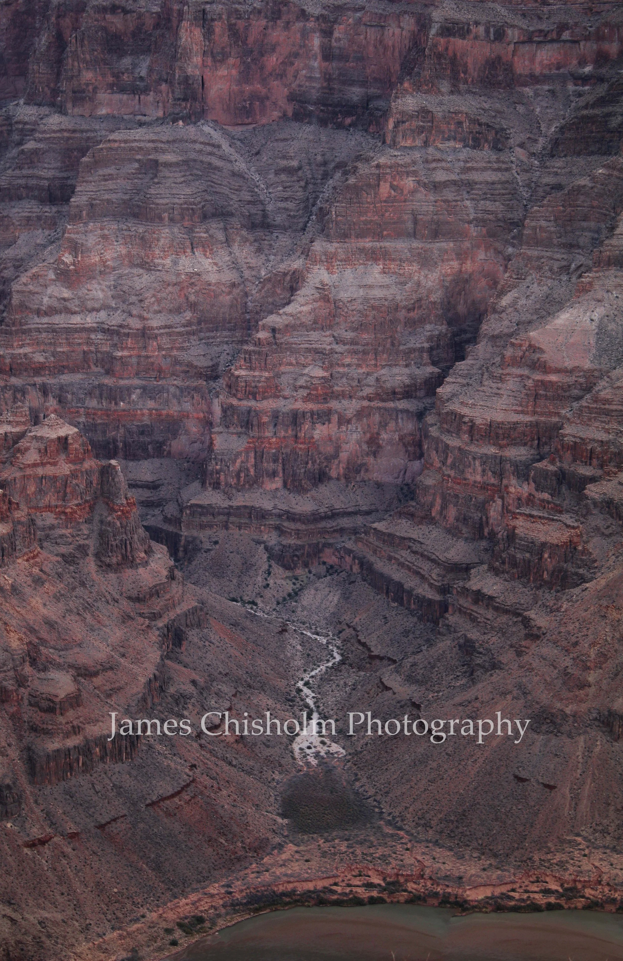A view of the Grand Canyon with layered rocks in shades of red, brown, and gray, and a river at the bottom.