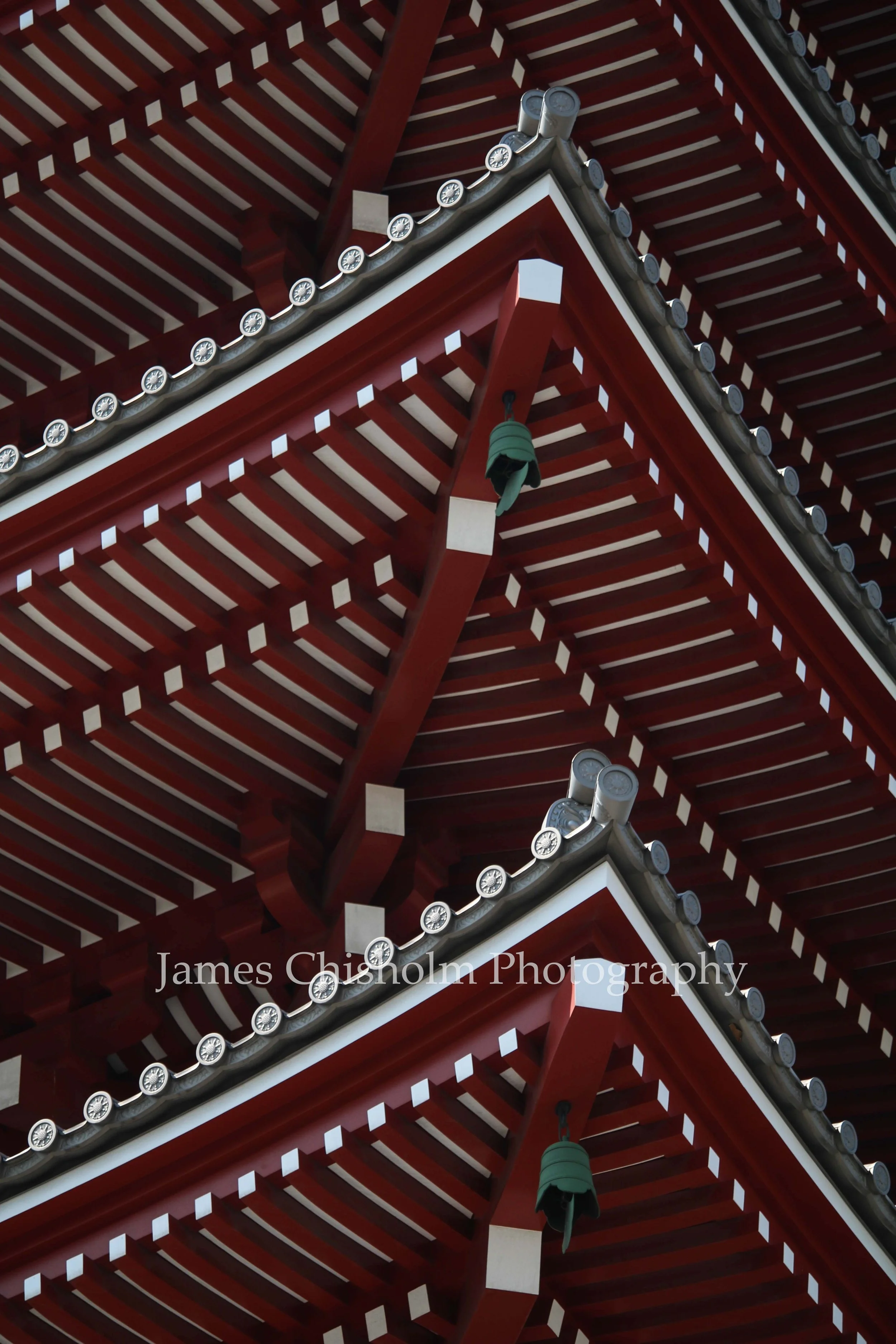 Close-up of the corner of a traditional Japanese temple roof, featuring wooden beams, decorative roof tiles, and hanging bells.