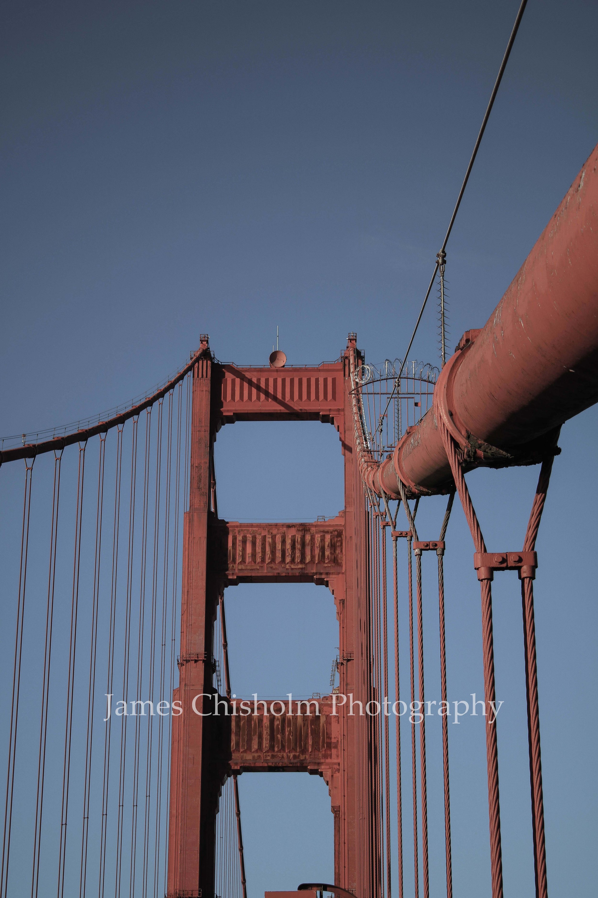 Lower part of the Golden Gate Bridge with cables and towers against a clear blue sky.