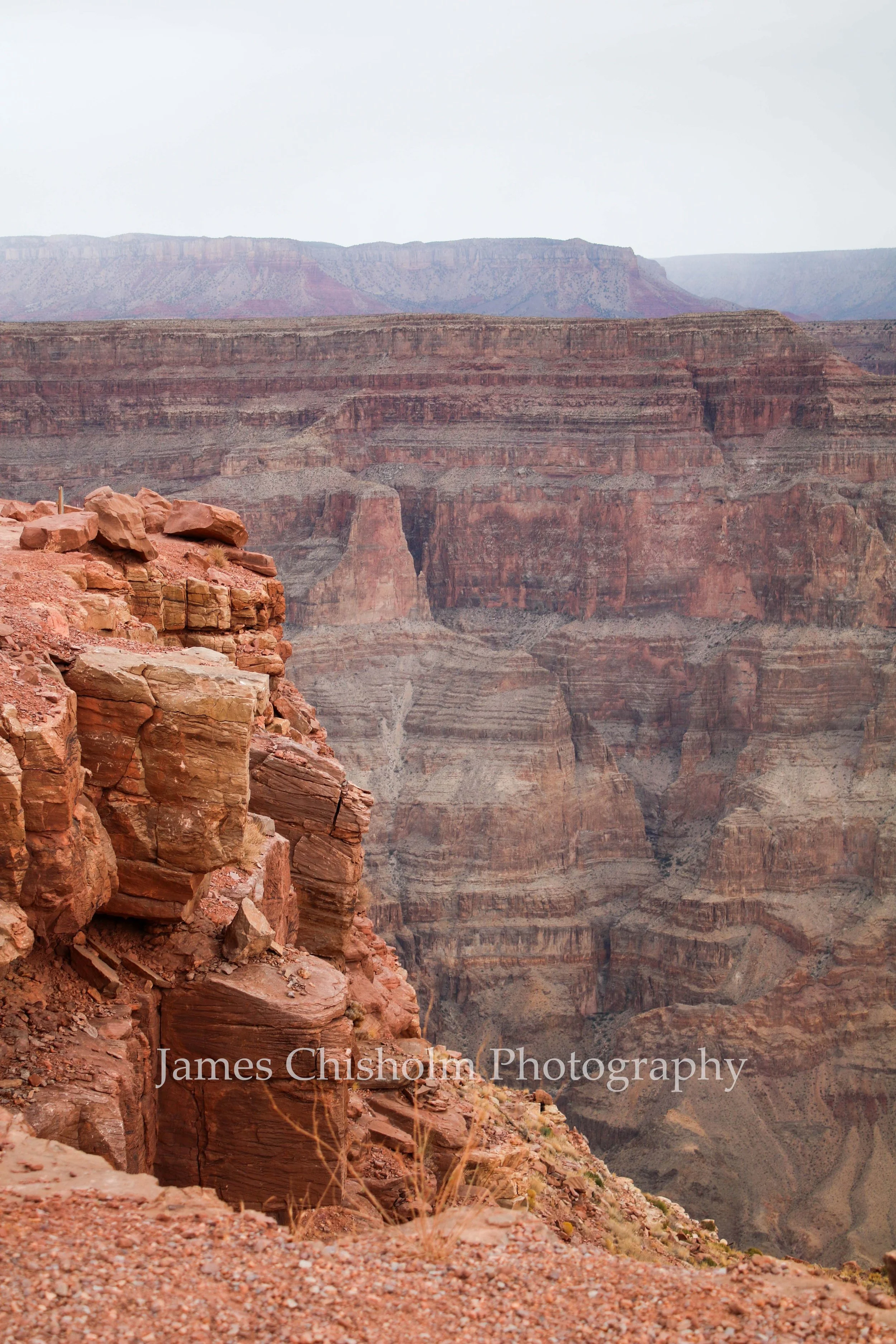 View of the Grand Canyon with layered red and brown rock formations under an overcast sky.