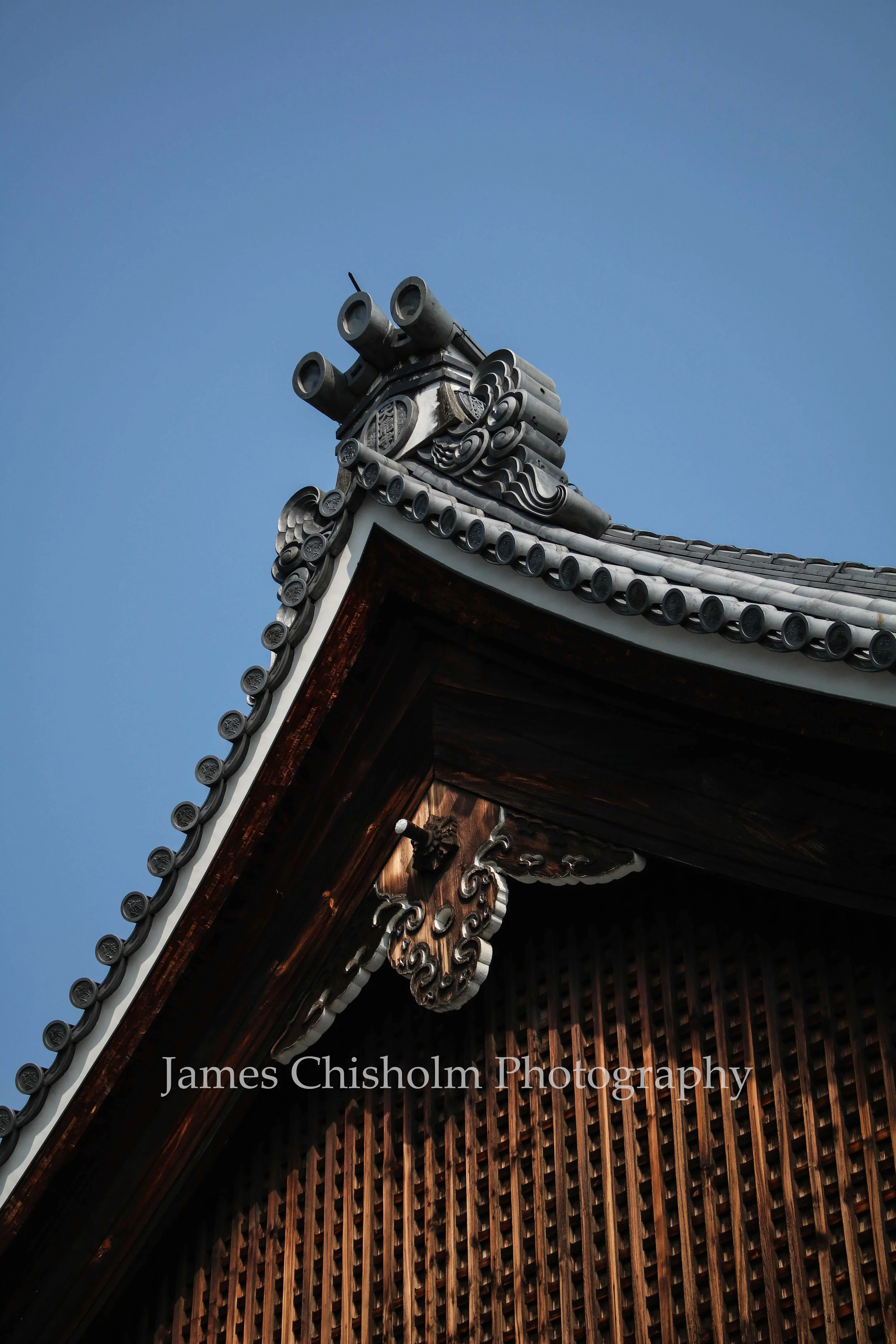 Close-up of a traditional Asian roof with ornate ceramic tiles and intricate wooden carvings against a clear blue sky.