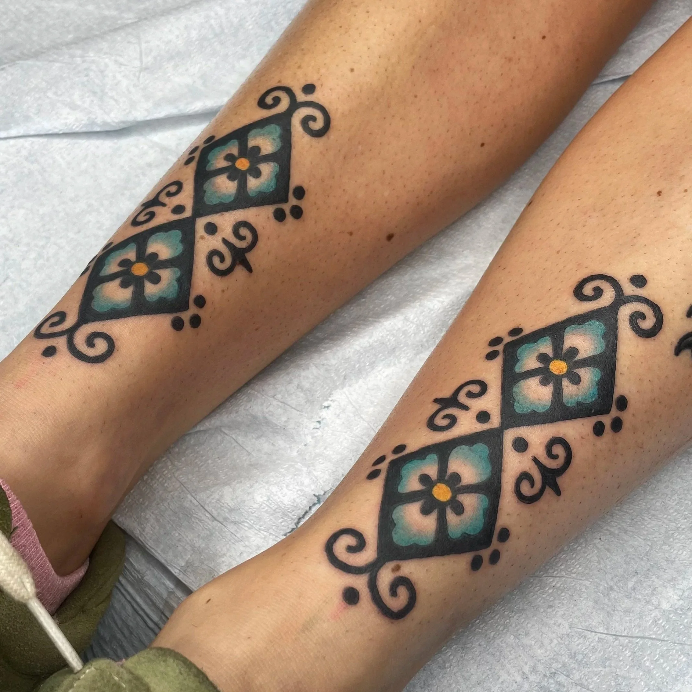 Close-up of a person's leg with a colorful ornamental tattoo and black decorative lines.