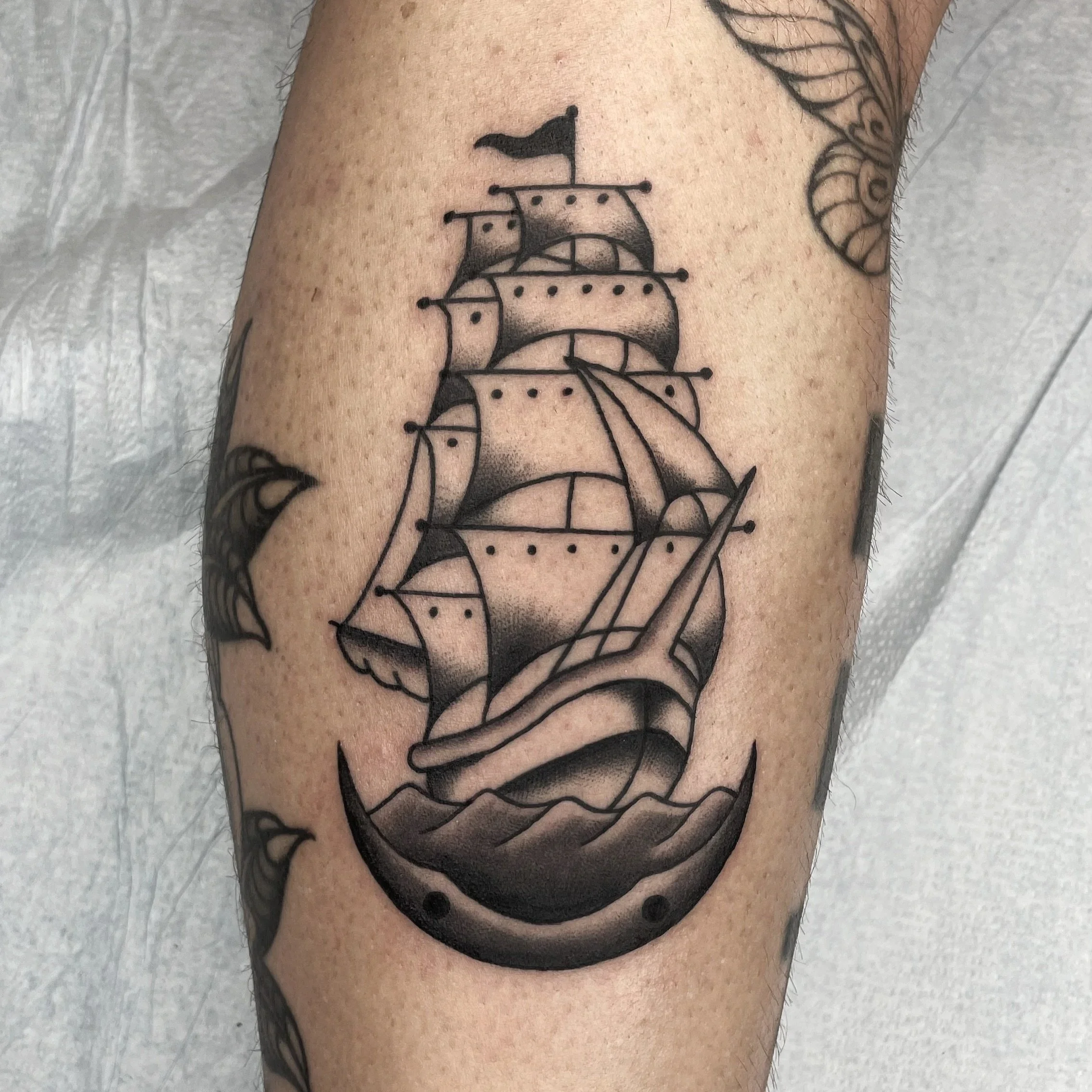 A tattoo of a classic sailing ship with sails and a flag on an individual's leg.