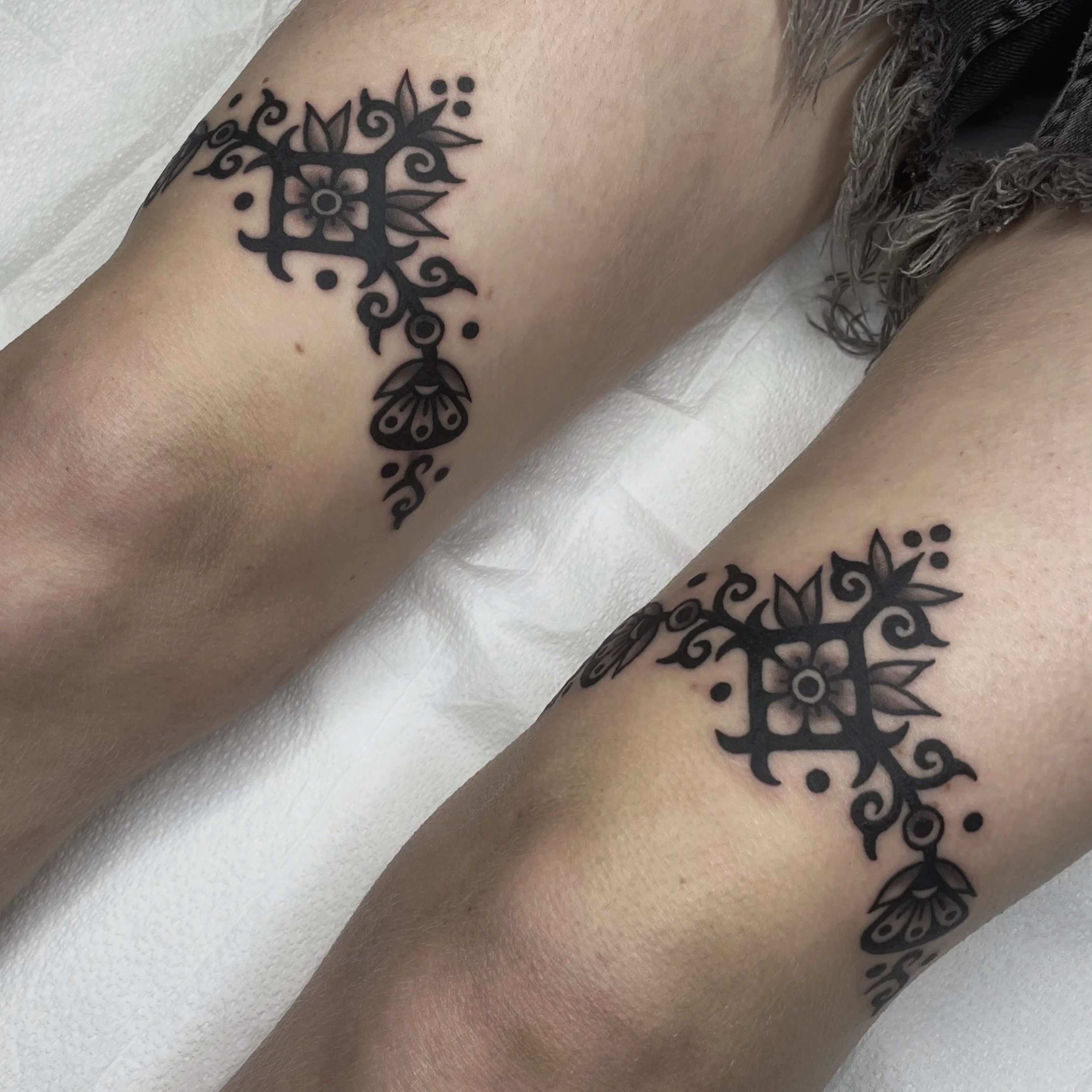 Close-up of a tattoo featuring a symmetrical black design with floral elements on a person's skin.