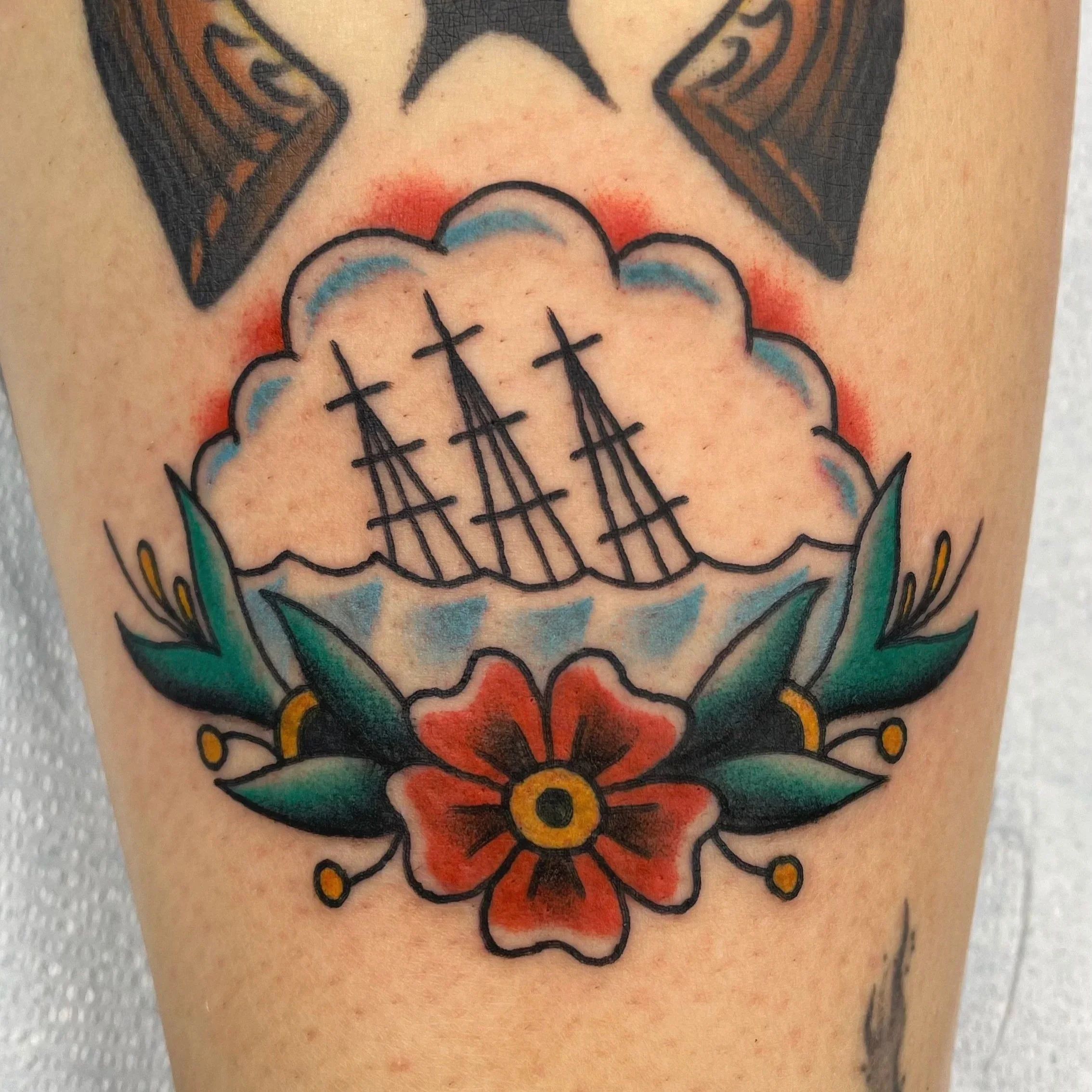 Close-up of a colorful tattoo on skin featuring a stylized cloud with red, orange, blue, and black outlines.