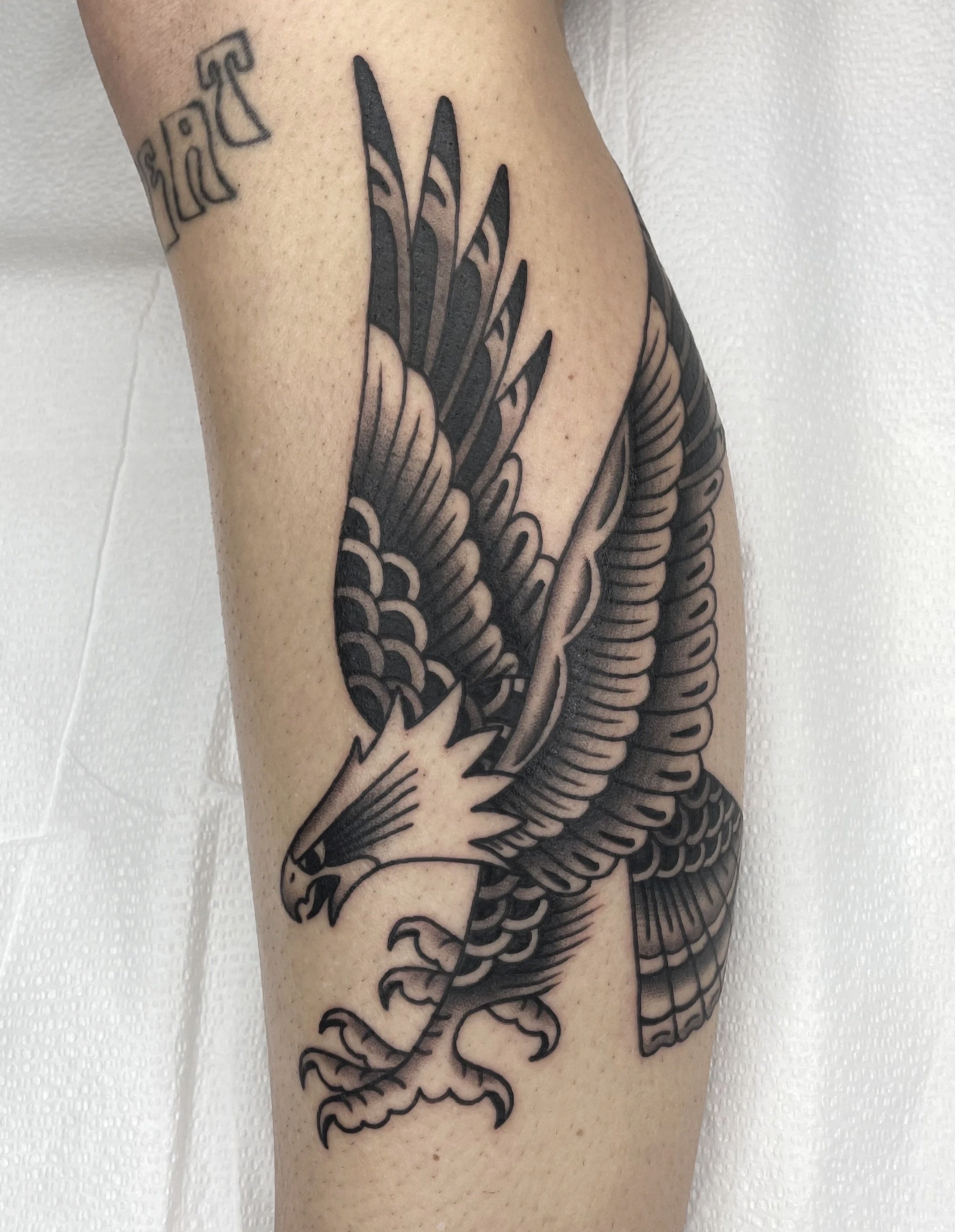Black and gray tattoo of an eagle on a person's arm, with detailed scales, claws, and wings, in a traditional style.