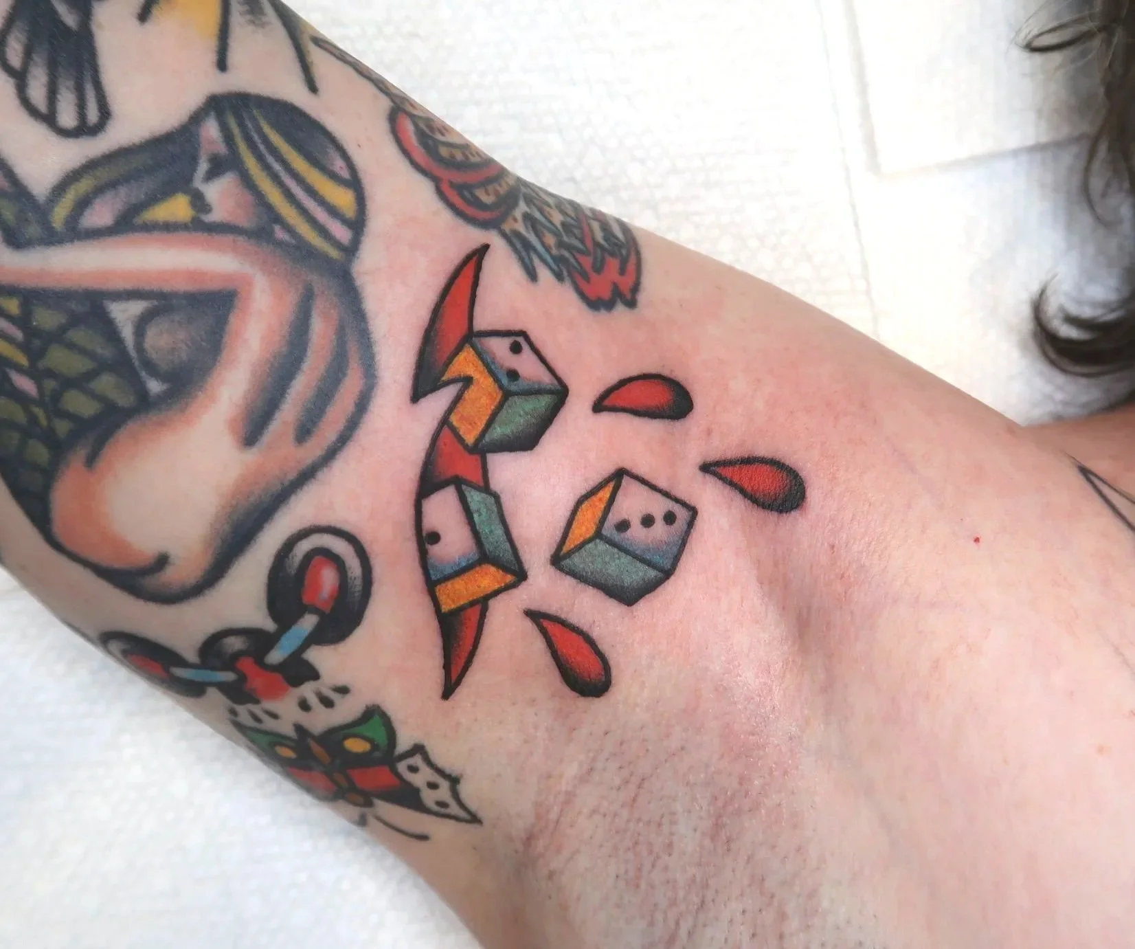 Tattooed arm with colorful dice and red teardrop shapes.