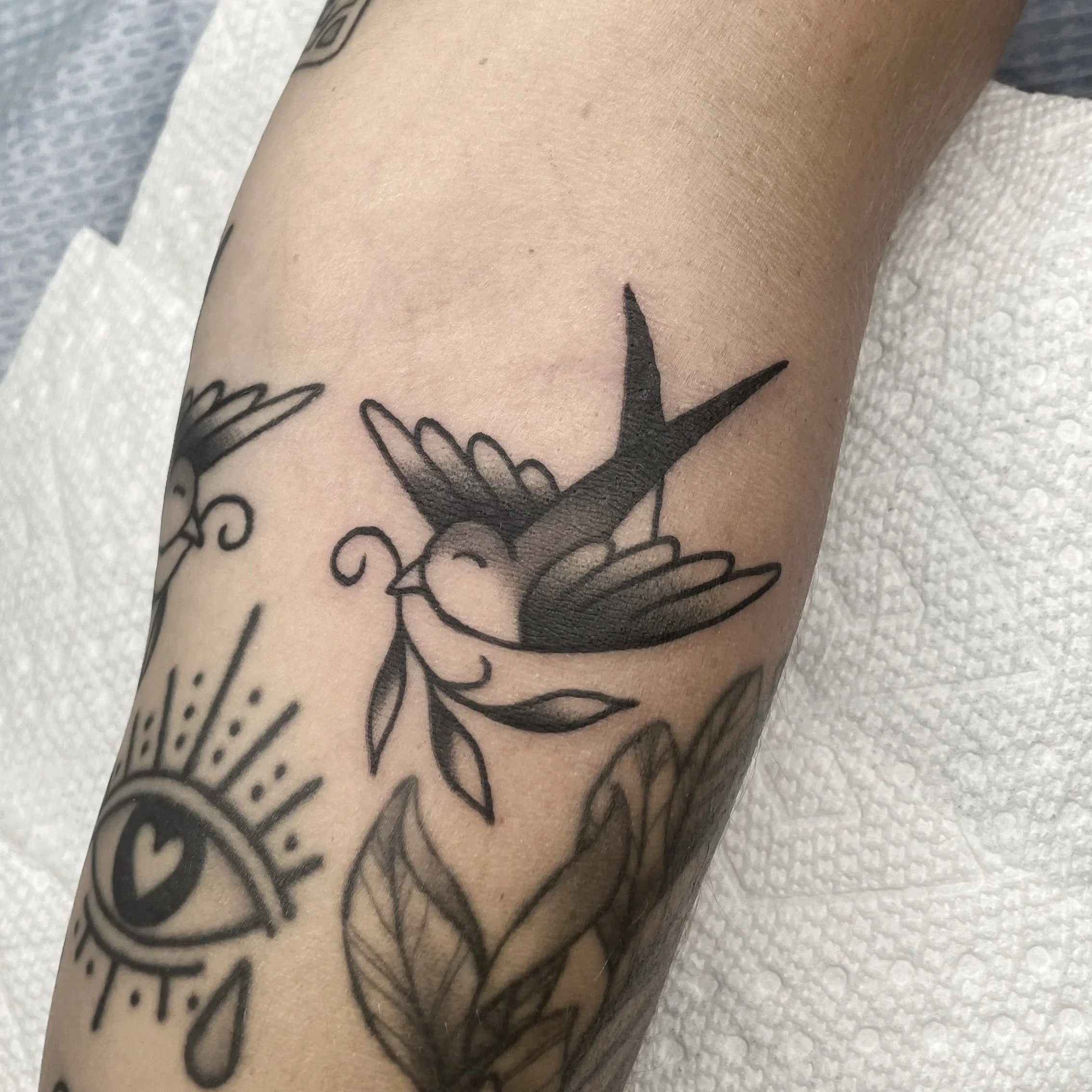 Close-up of a tattooed arm with a black ink design on light skin, resting on a white textured surface.