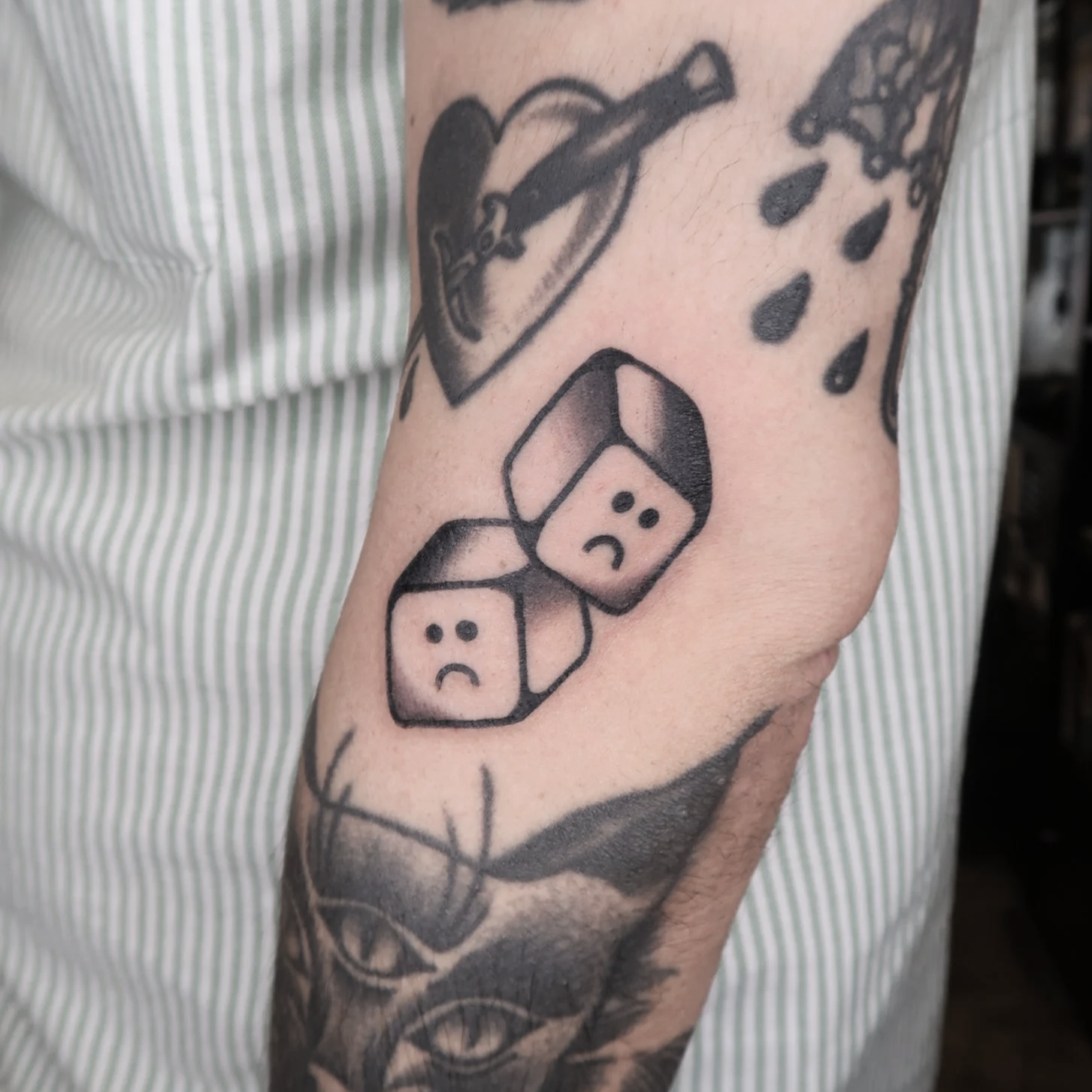Tattoo of two sad face dice on a person's arm, with other tattoos partially visible.
