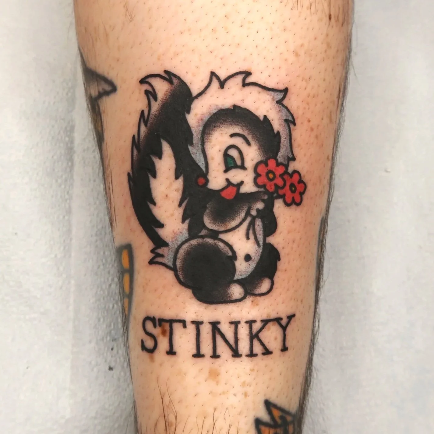 Tattoo of a skunk holding a red flower, with the word 'STINKY' written underneath.