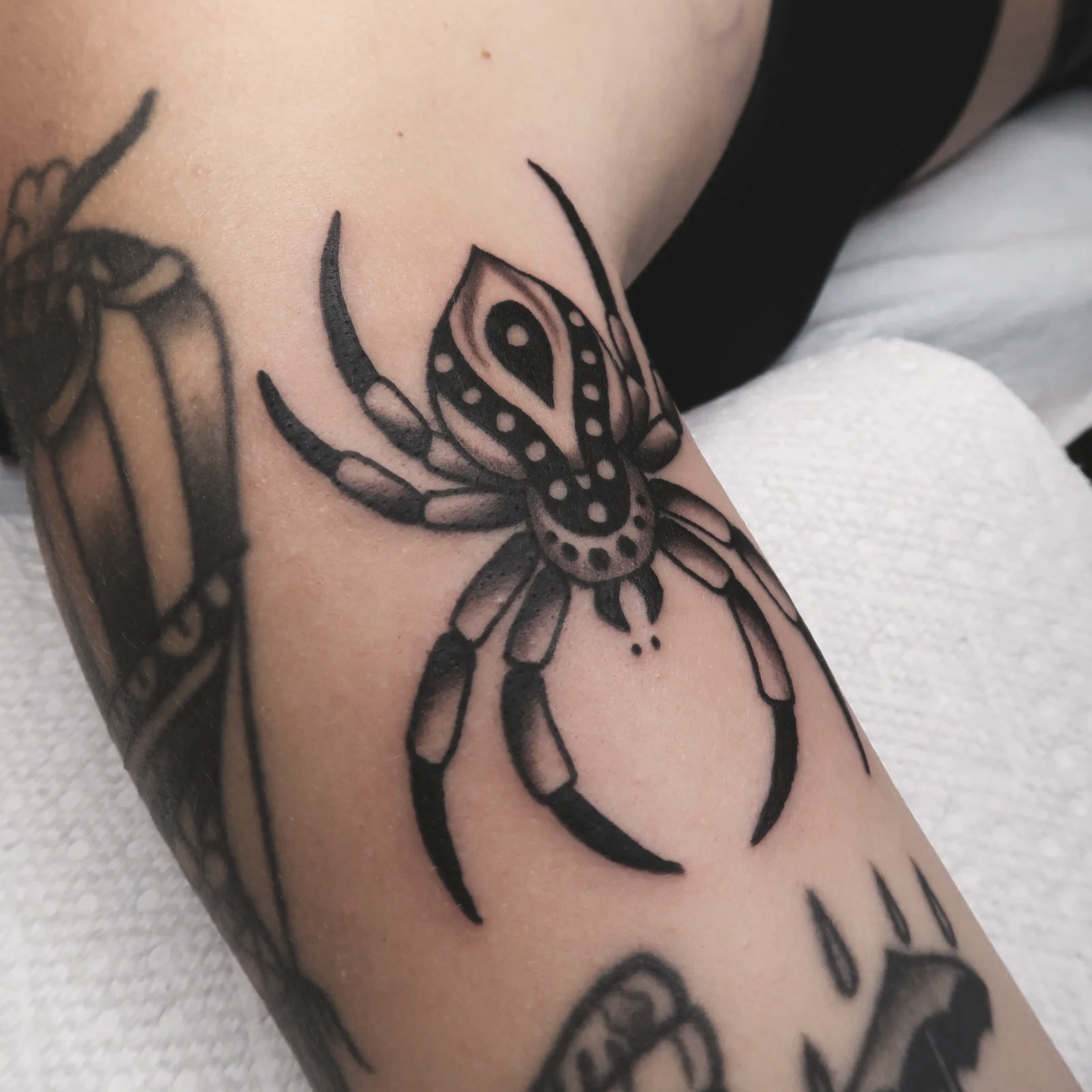 Close-up of a black tattoo of a spider on a person's skin.