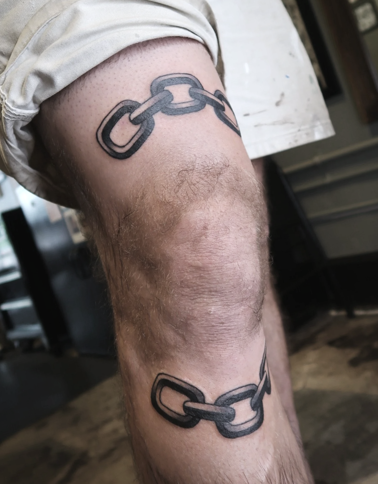 Tattoo of a black chain link on a person's leg.