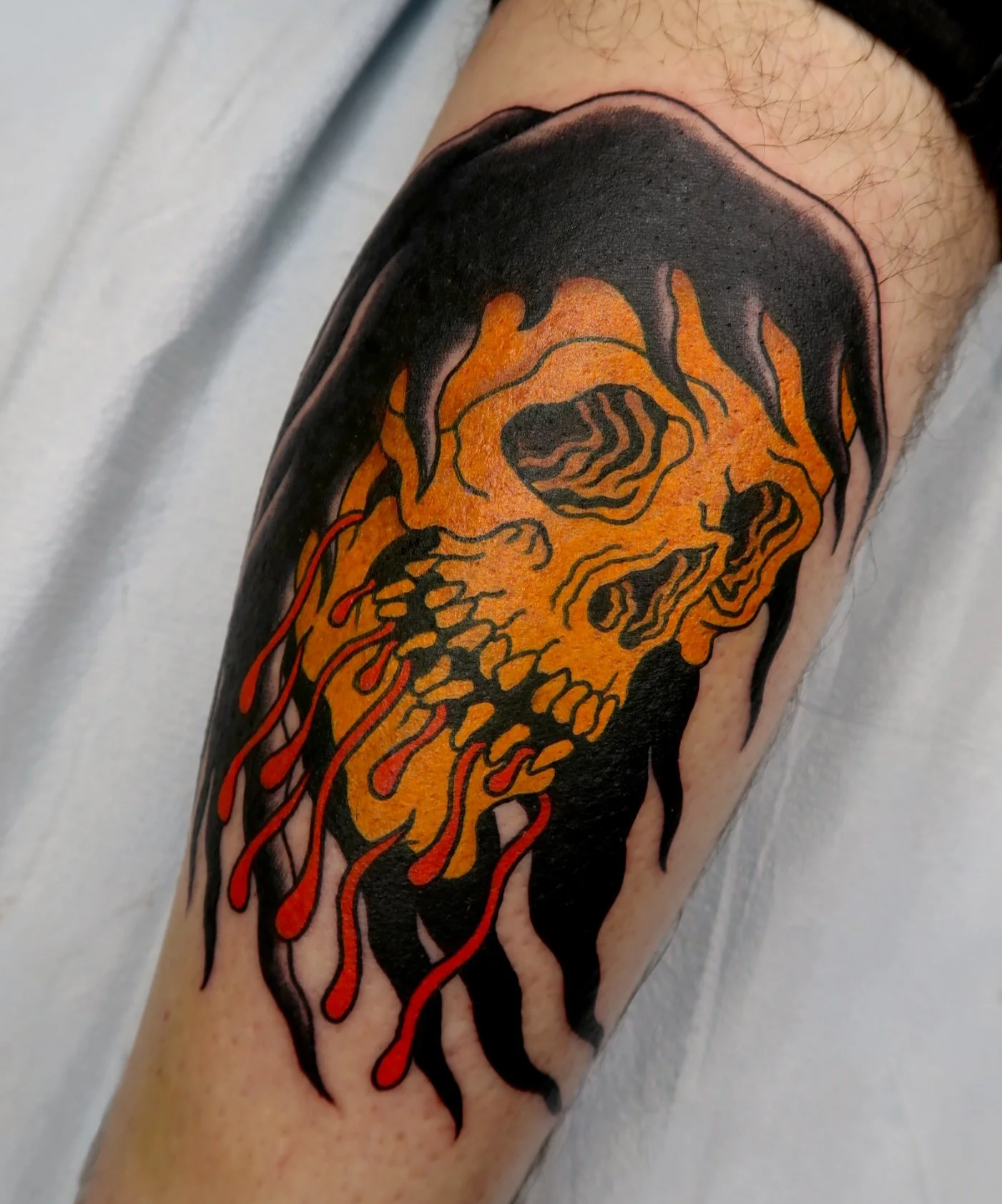 Tattoo of a flaming skull on a person's arm with orange, black, and red ink.