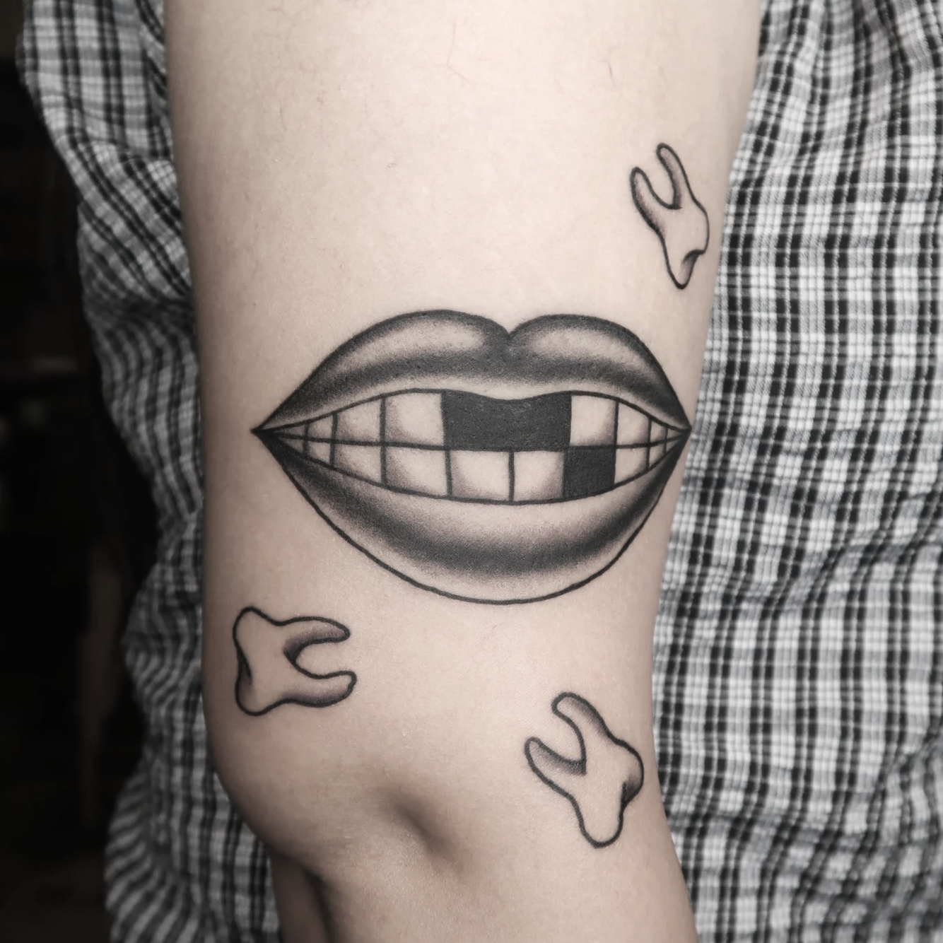 Tattoo of a large pair of lips with a missing teeth on the person's upper arm, surrounded by smaller teeth.
