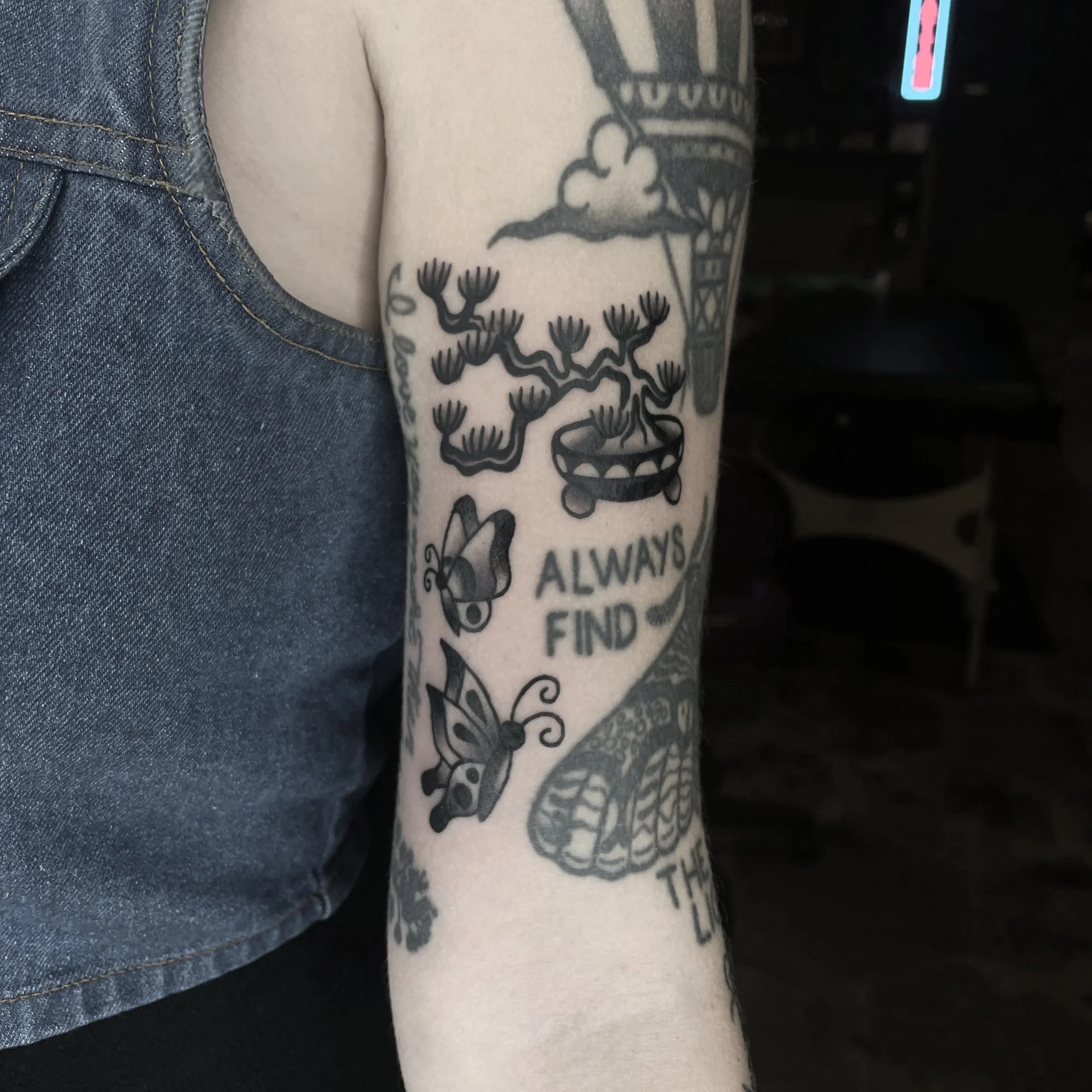 Close-up of a tattoo on a person's arm featuring a bonsai tree and butterflies.