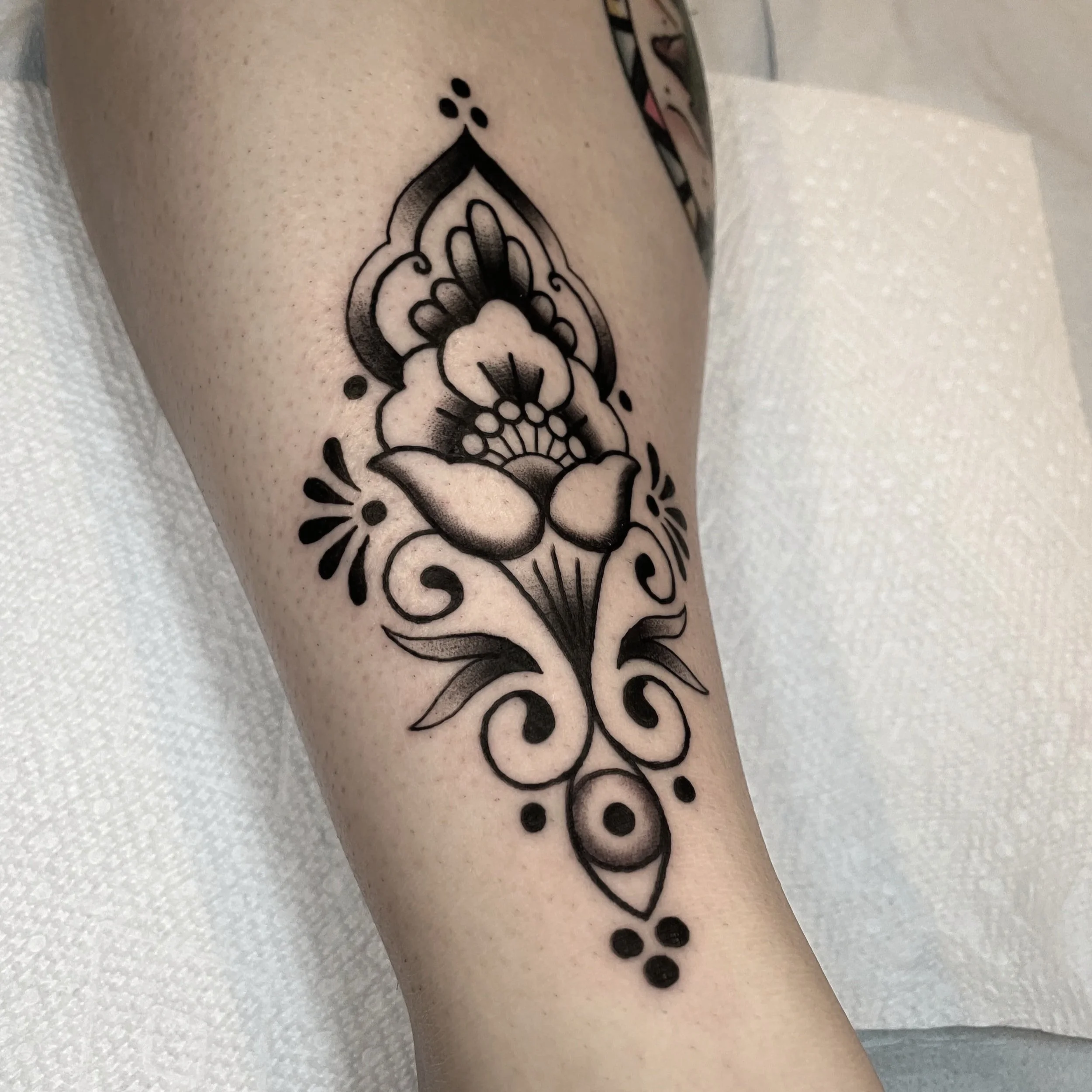 Black line art tattoo of a flower with decorative elements on a person's skin.