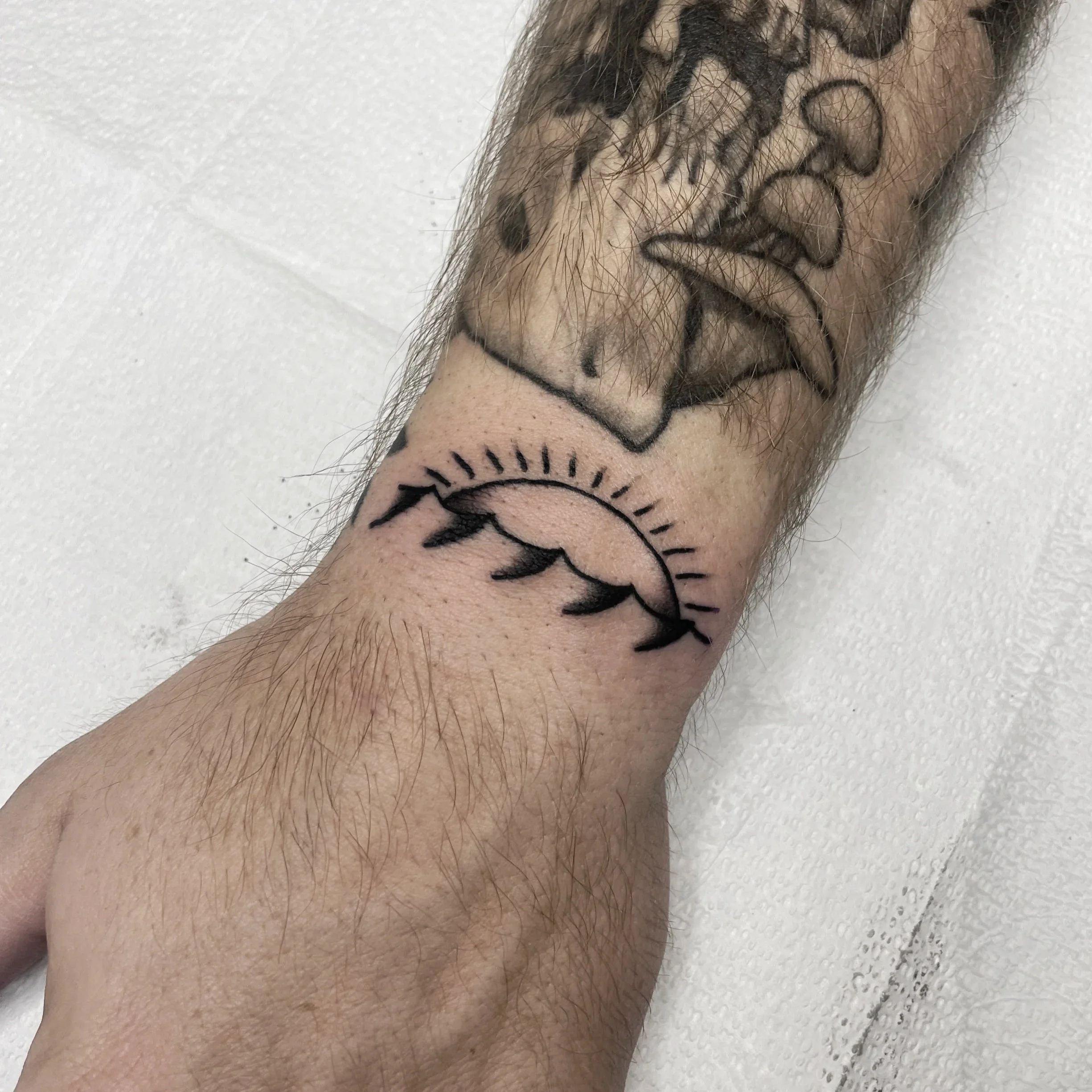 Close-up of a person's arm with a black ink tattoo of a star outline, surrounded by fine arm hair and a light skin tone, lying on a white textured surface.