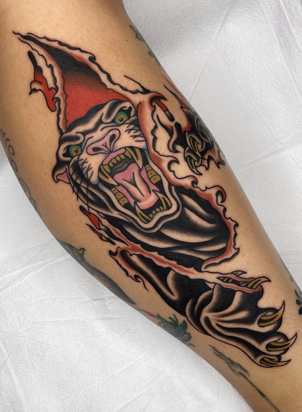 Tattoo of a fierce panther with emerald green eyes, snarling with claws extended on a person's arm.