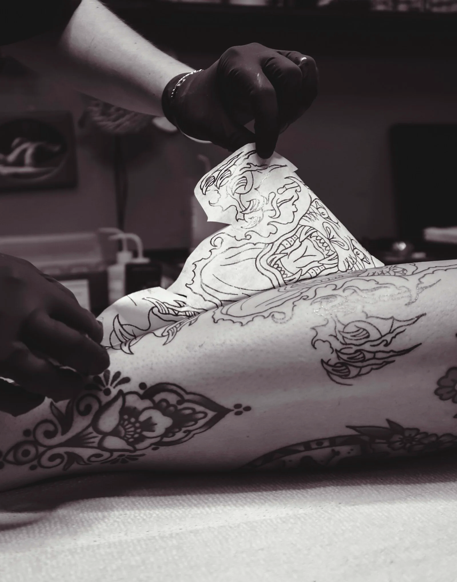 A person wearing black gloves is placing a tattoo stencil