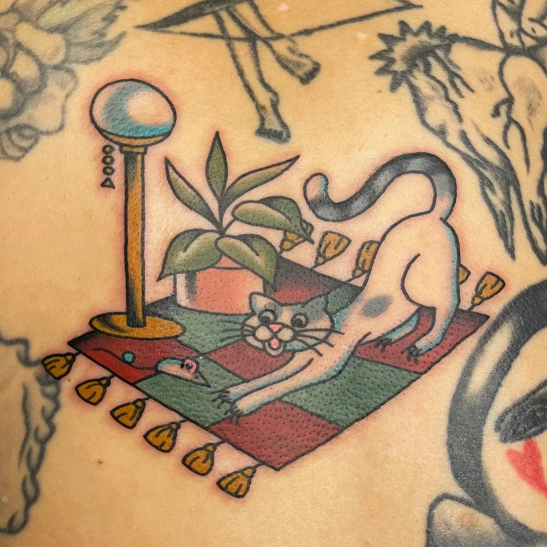 Close-up of a colorful tattoo on skin featuring a cat in a living room scene.