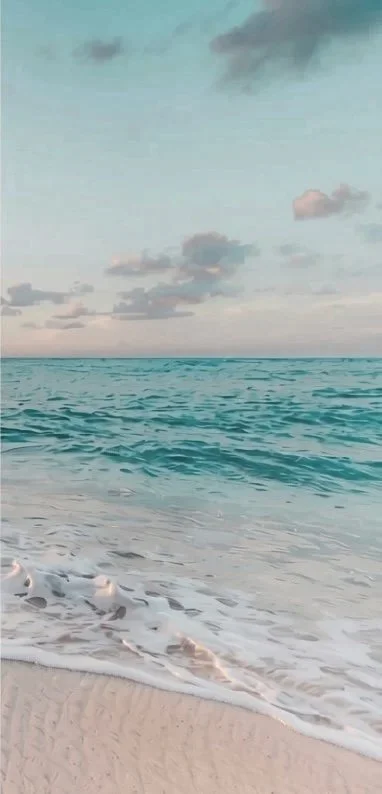 A beach scene with gentle waves hitting the sandy shore, under a partly cloudy sky