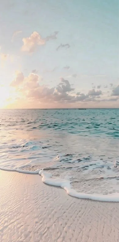 Sunset over the ocean with waves gently reaching the sandy beach and scattered clouds in the sky.