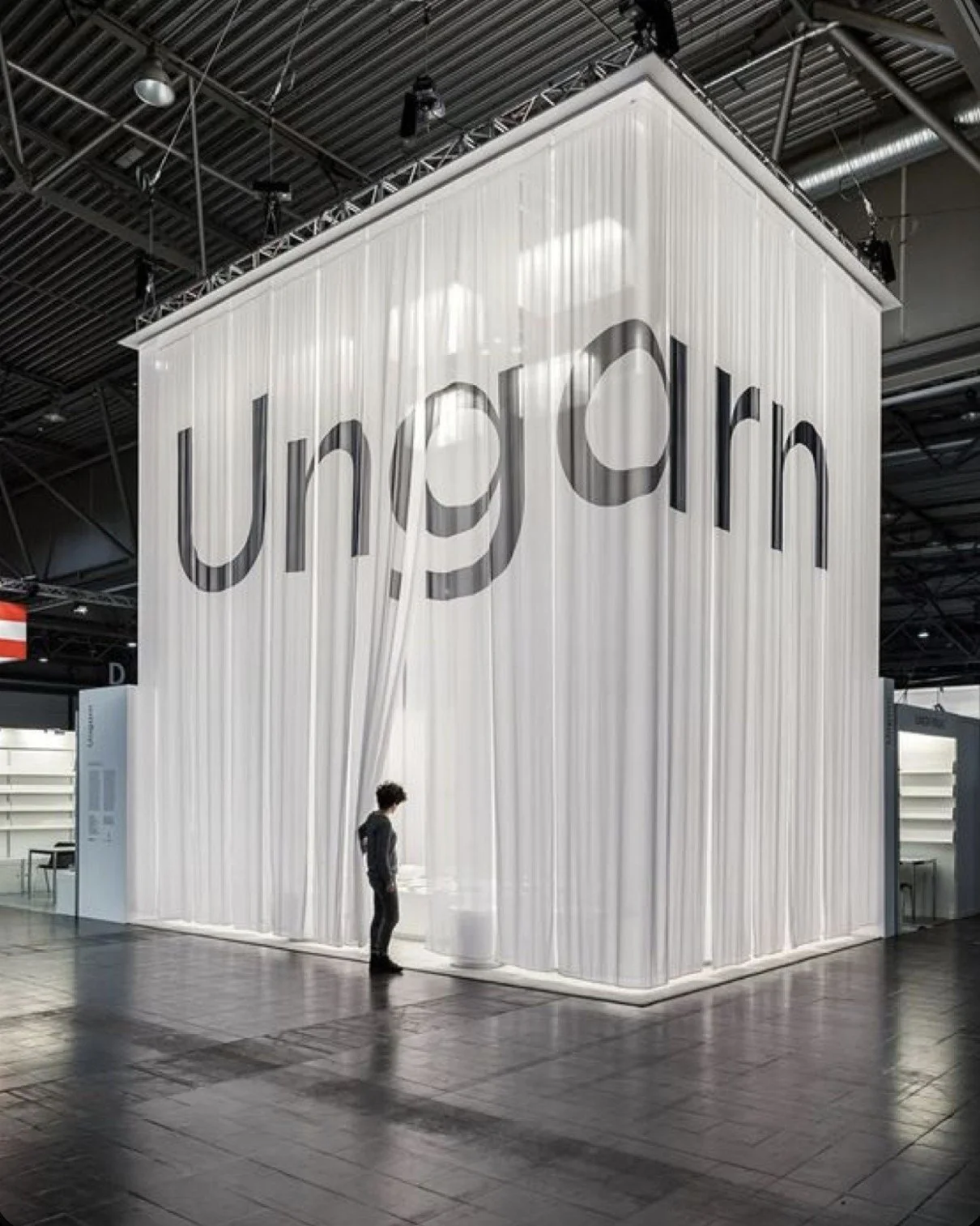Large white exhibition booth with the word 'Uber' in black letters, partially obscured by white curtains, inside a convention center with a person standing in front.