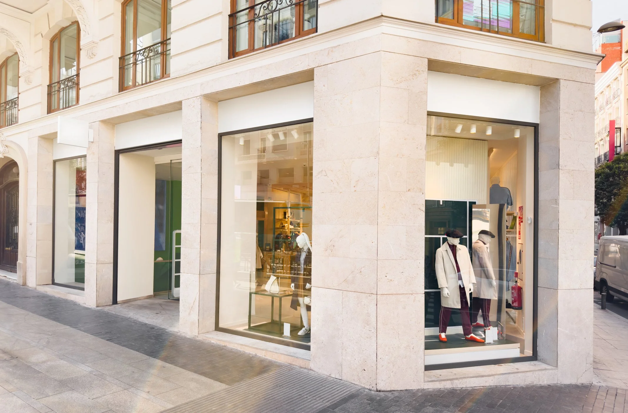 Modern fashion boutique storefront with large glass windows displaying mannequins dressed in stylish clothing, on a city street corner.