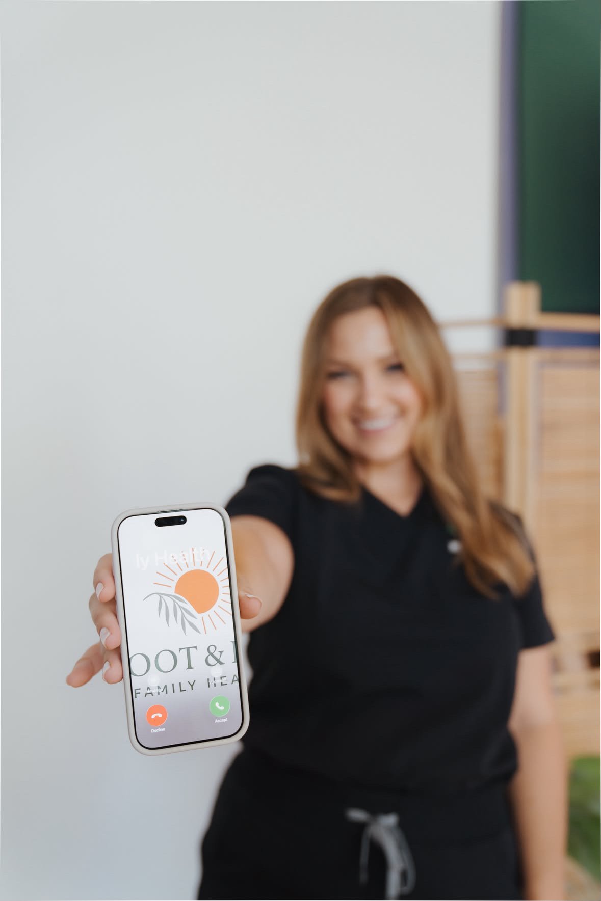 A woman smiling and holding a smartphone with a caller ID display showing the logo and name of 'Foot & Family Health'.