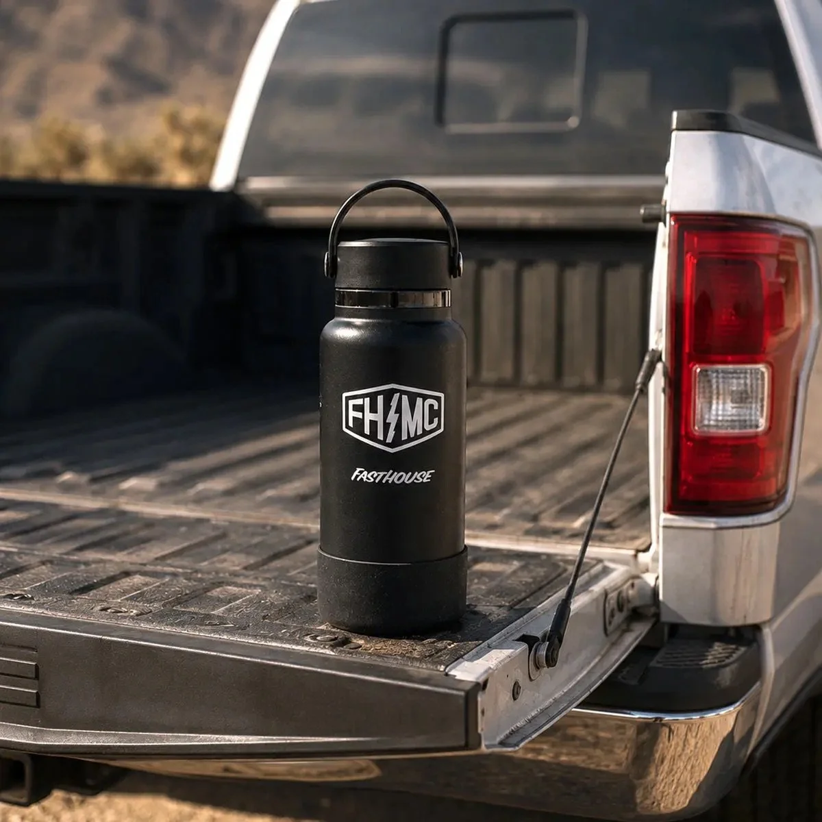 Black water bottle with a logo and the word faster on the truck bed of a pickup truck.