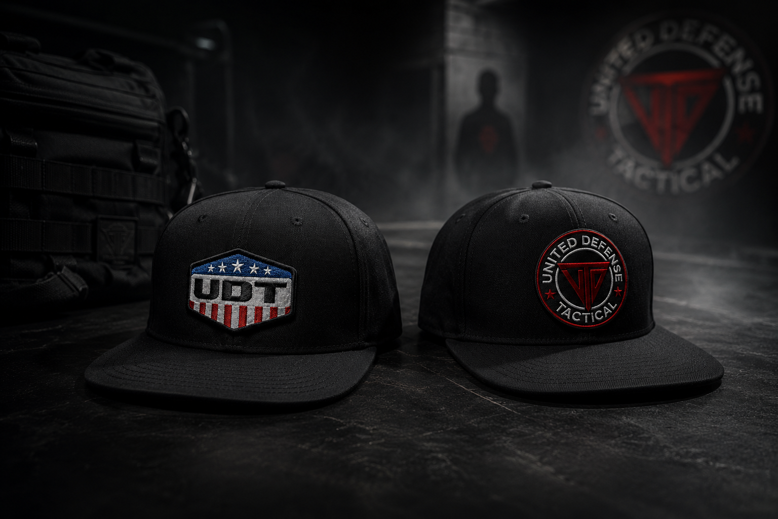 Two black tactical caps with patches, one reading 'UDT' with patriotic stars and stripes and the other reading 'United Defense Tactical', placed on a dark surface with a tactical bag and a blurred background.