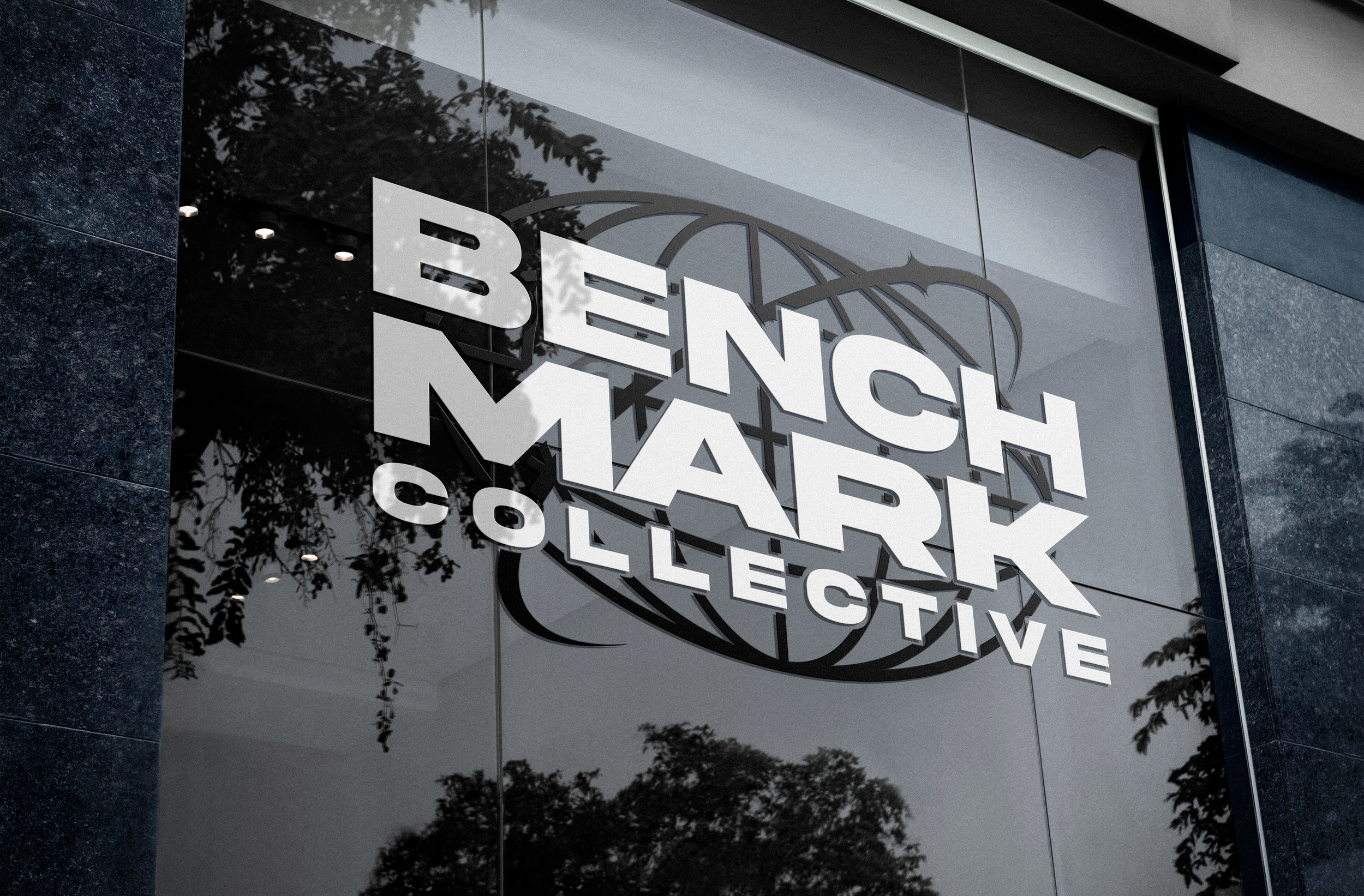 Close-up of a storefront display with the text 'Brennan Machinery' in large, white letters on a reflective glass surface, with tree branches and sky reflected in the glass.