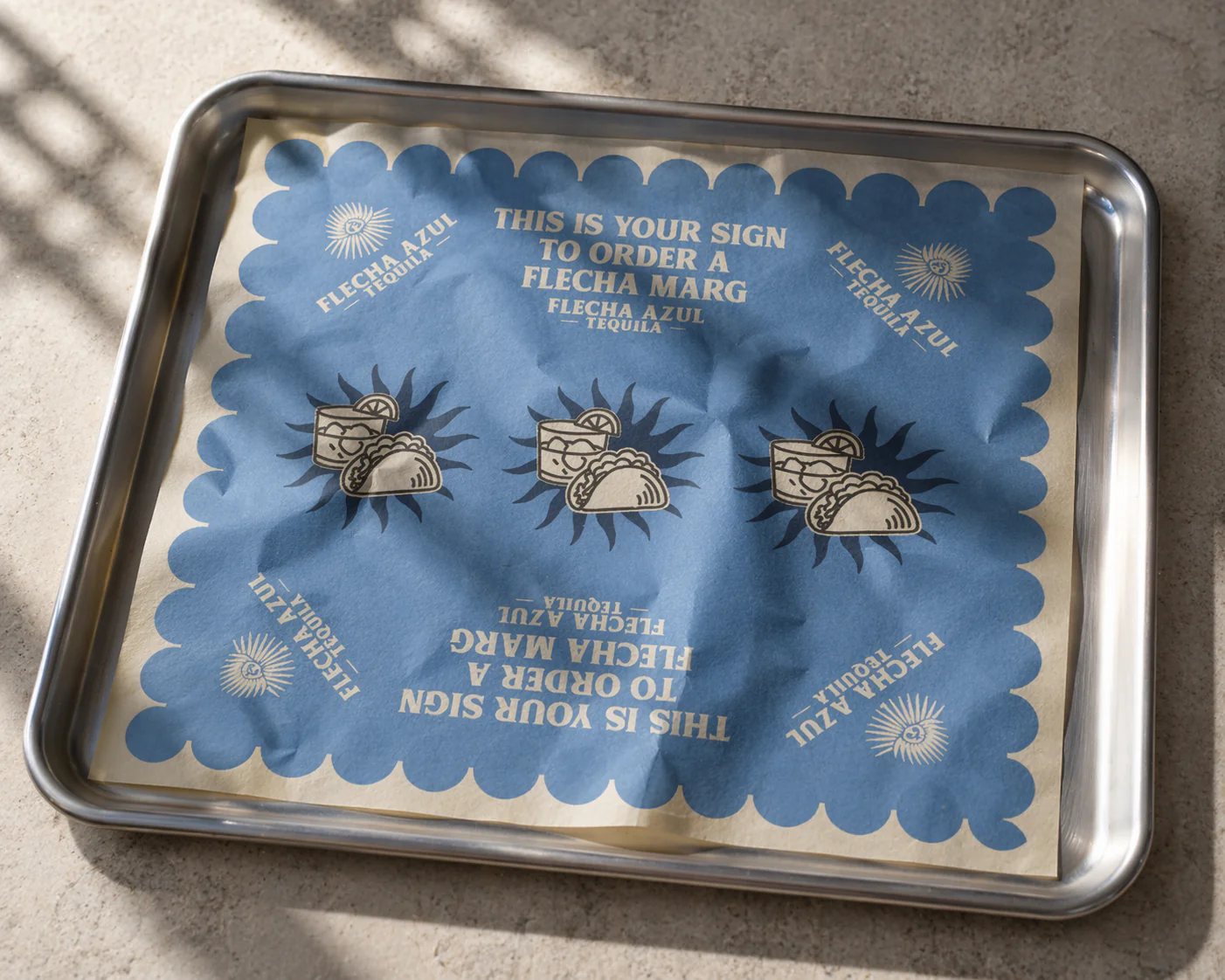A metal tray with a blue and beige paper liner that has writing and illustrations for ordering drinks at a restaurant, featuring the phrase 'This is your sign to order a Flecha Marg' and images of tacos, tequila, and a lemon wedge.