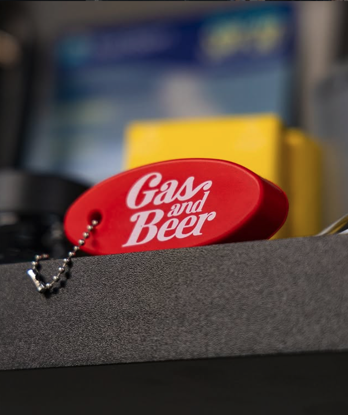 Red tag with white text saying "Gas and Beer" resting on a surface with a blurred background.