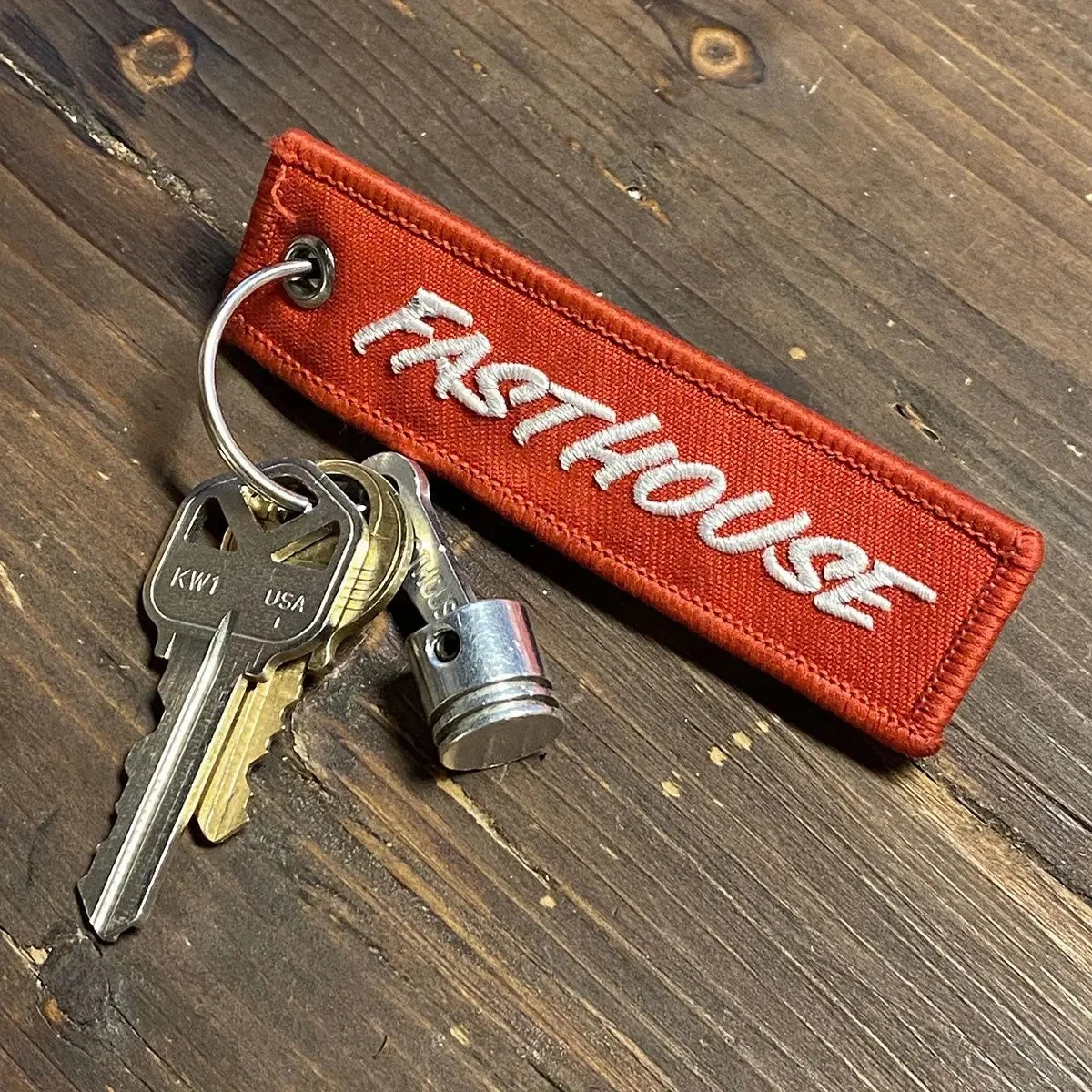 A set of keys attached to a metal key ring, a small cylindrical object, and a fabric keychain with the words 'FIREHOUSE' embroidered on it in white, all placed on a wooden surface.