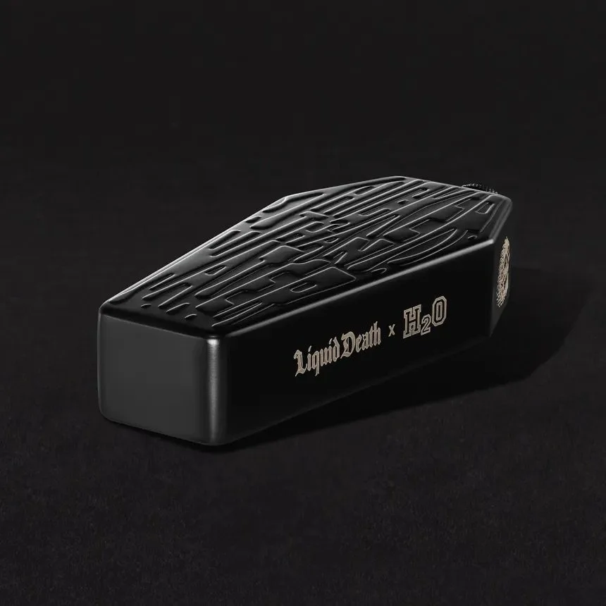 A black lighter with the phrase 'Liquid Death x H2O' written on the side, resting on a black surface against a black background.