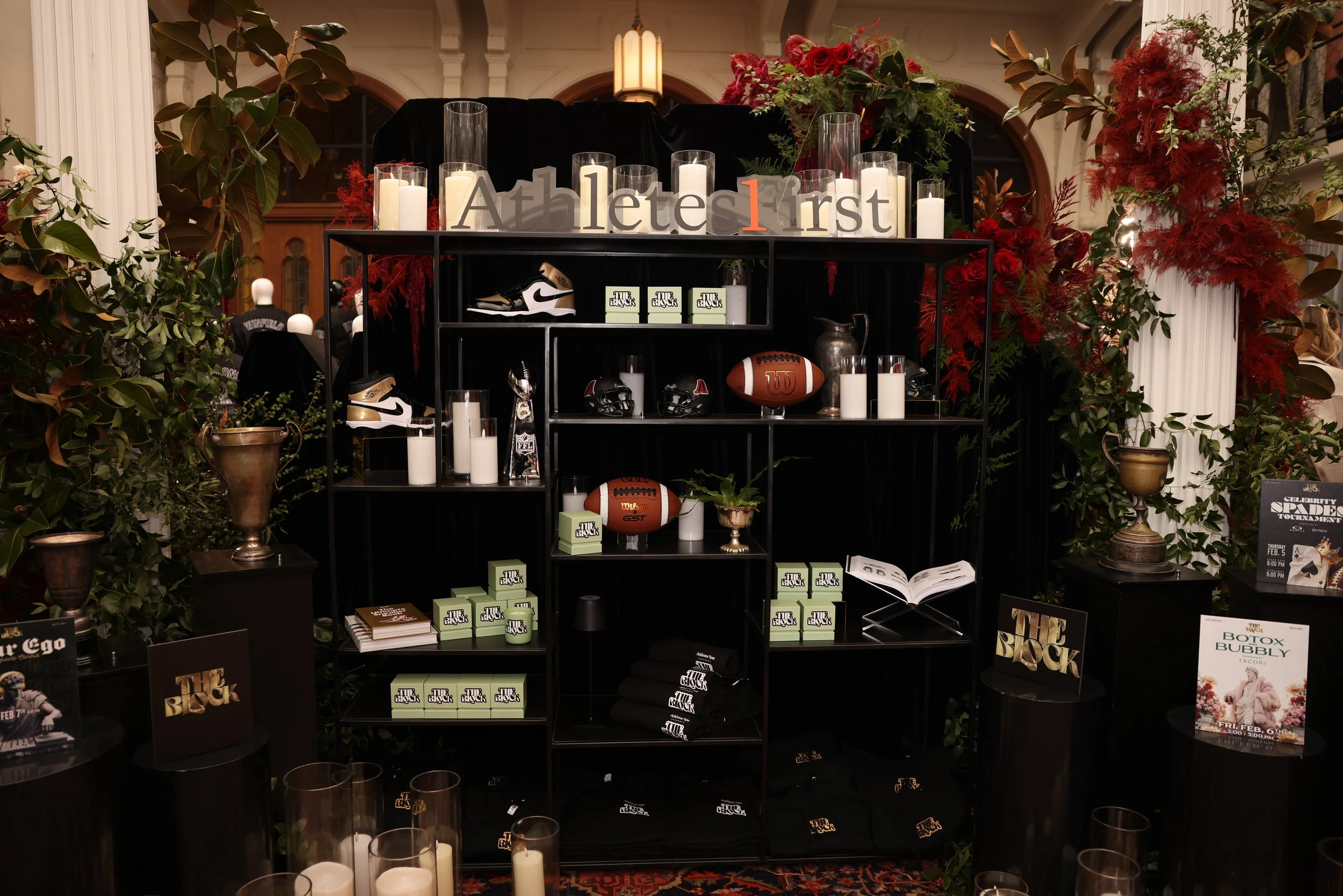 Display of various items related to football and sports, including sneakers, a football, and plaques, surrounded by candles and plants, with a sign that says 'Athletes First' on a shelf.