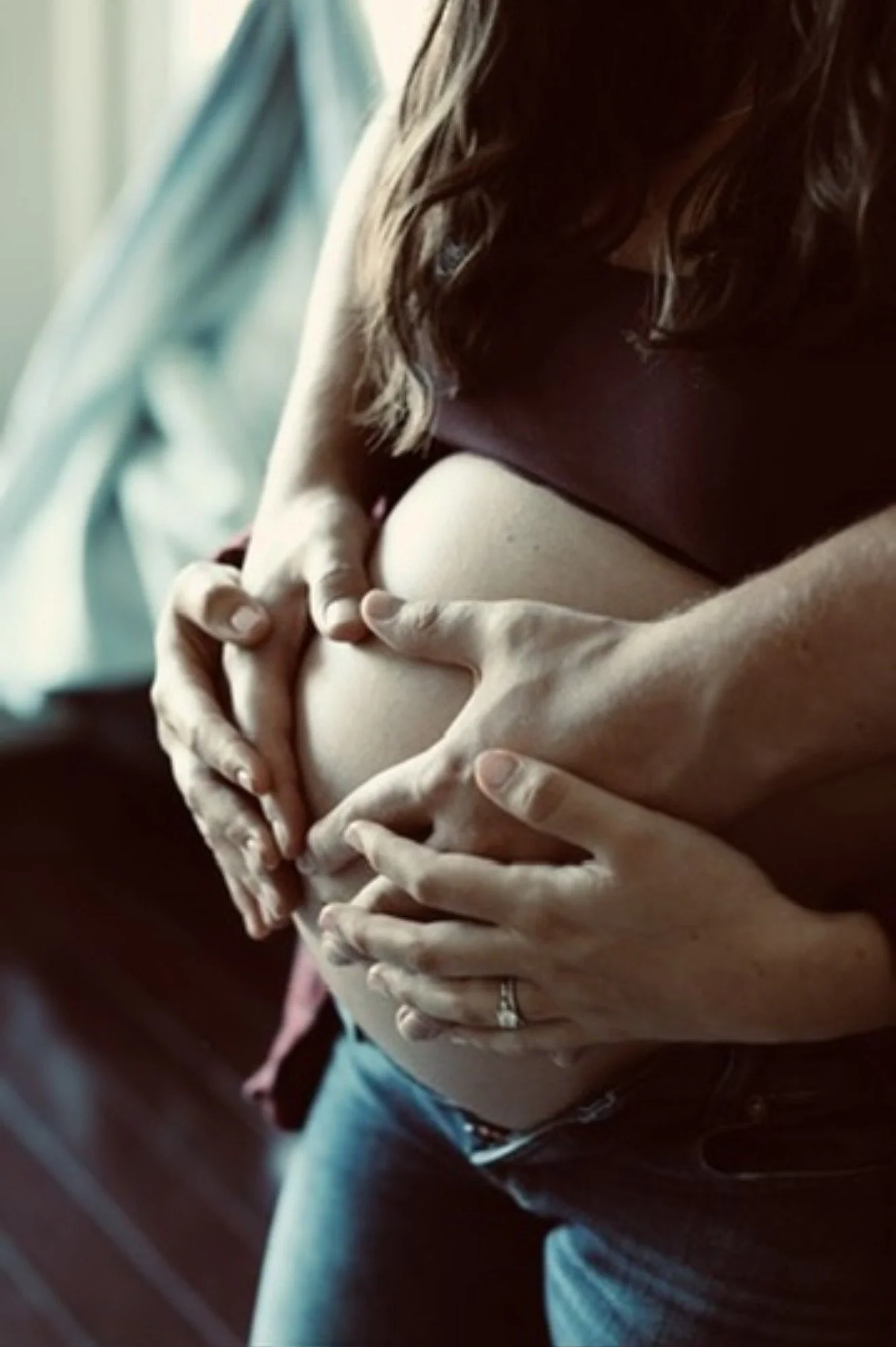 Close-up of affectionate hands holding a pregnant woman's belly.