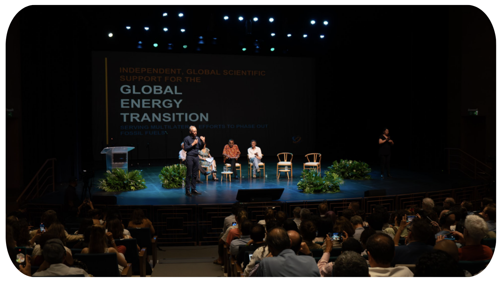 People attending a conference on energy transition, with speakers on stage and a large screen displaying the event's theme.