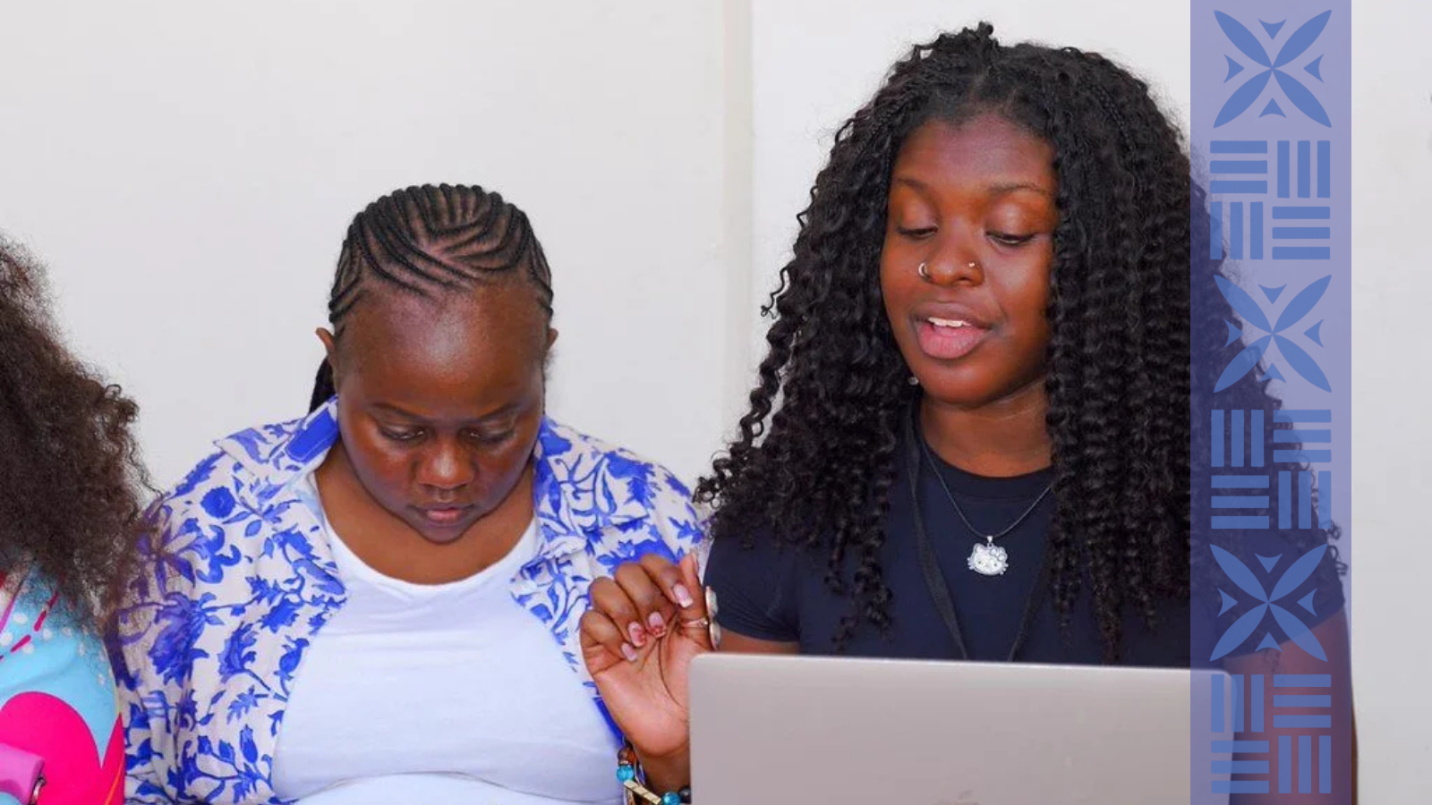 Two women sitting side by side, looking at a laptop screen, engaged in a discussion or activity, with a plain white wall in the background.